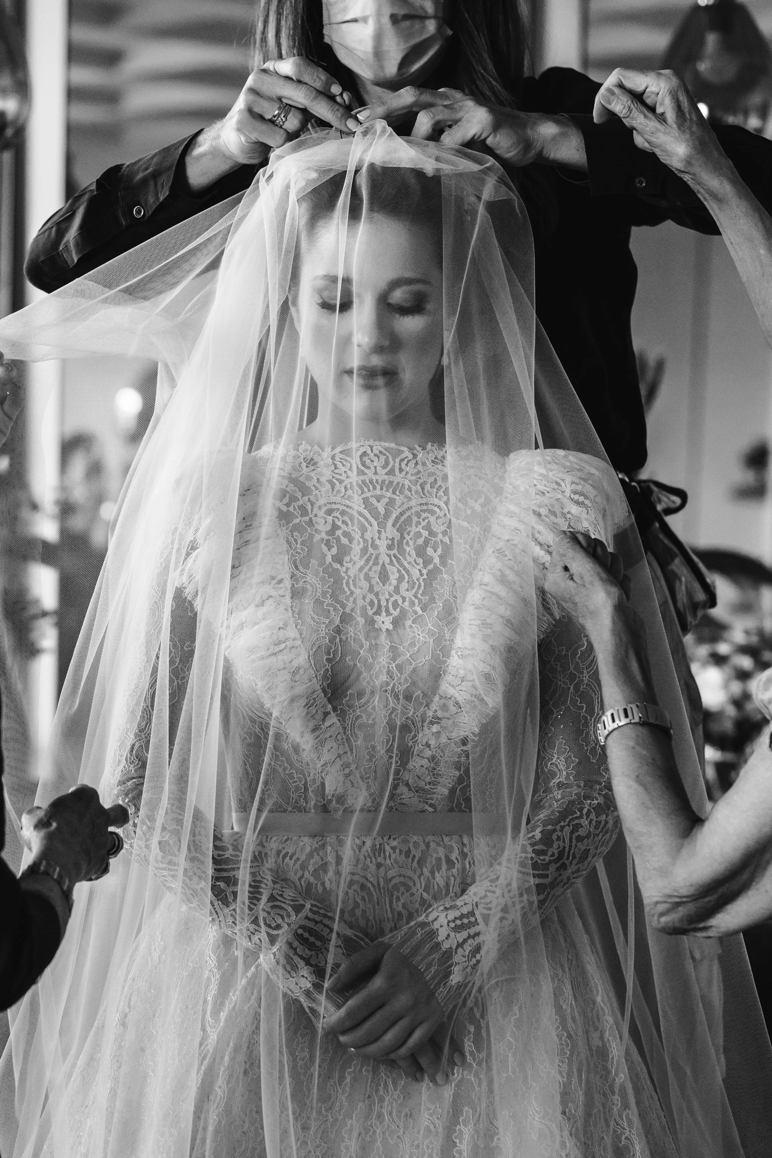 Una novia se prepara para su boda, rodeada de varias personas que la ayudan con su velo y vestido.