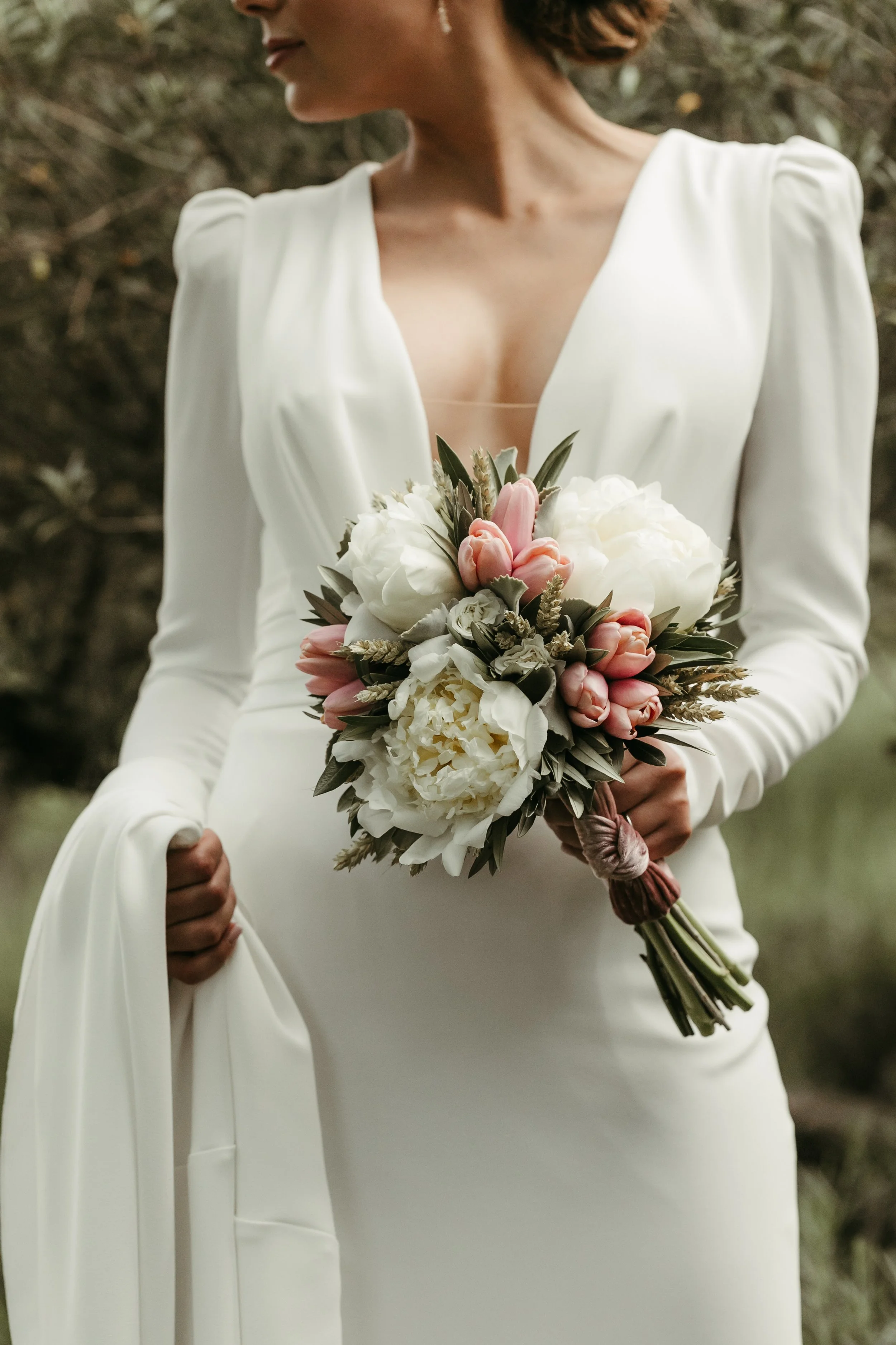 Una mujer de vestido de novia blanca sostiene un ramo de flores en un entorno natural.