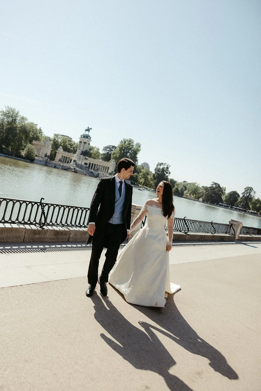 Bride and groom walking hand in hand along a lakeside promenade during their post-wedding session