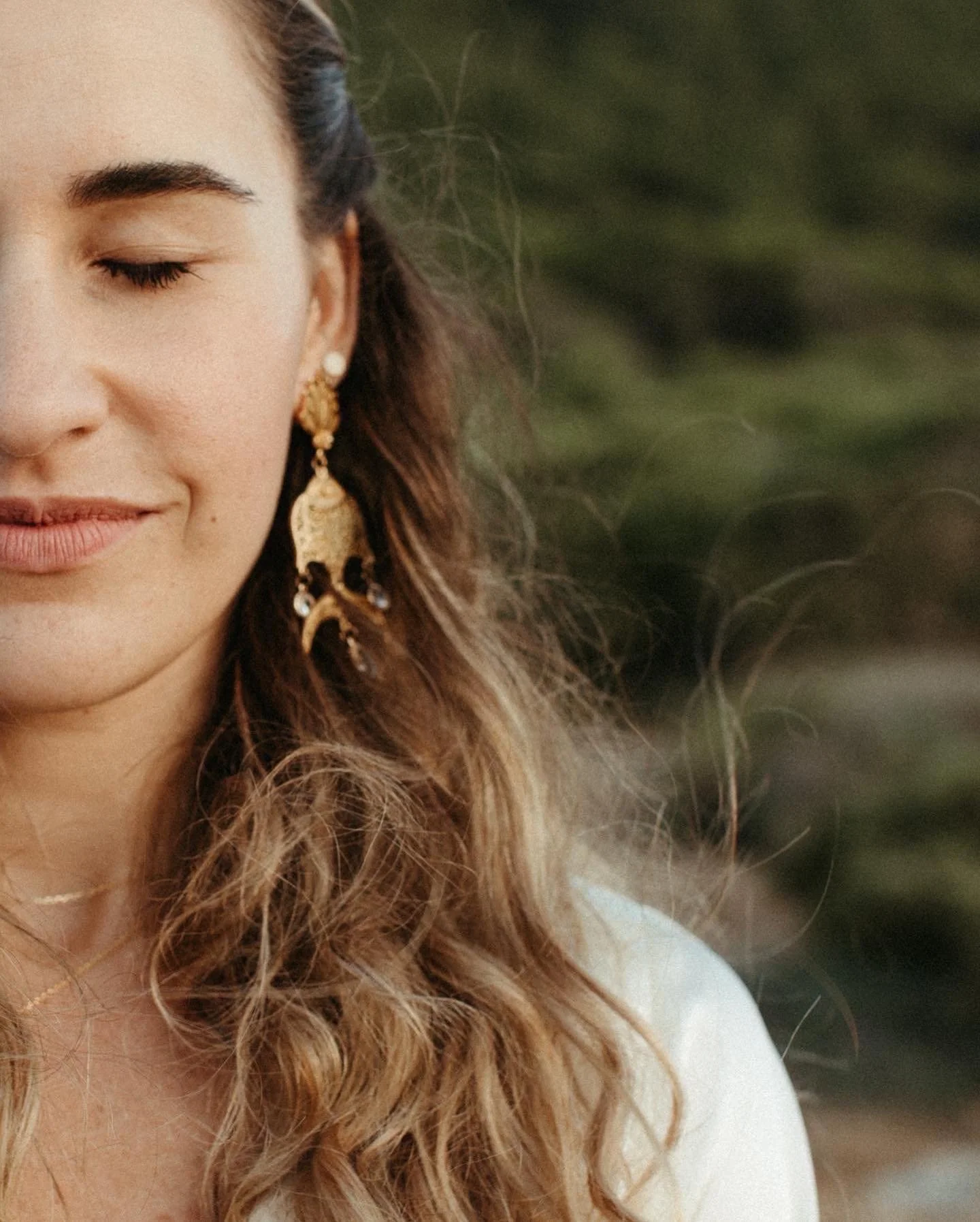Mujer con pendientes grandes de estilo tradicional y cabello rizado, con los ojos cerrados, en un entorno natural.