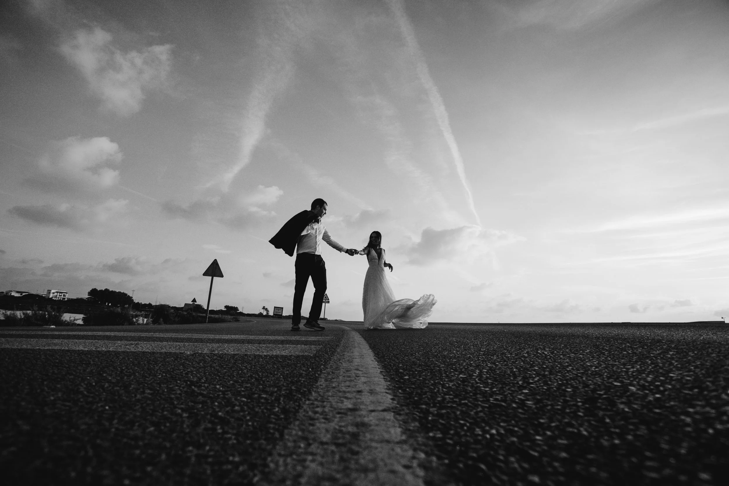 Pareja de novios caminando en una carretera en un atardecer, en la imagen en blanco y negro.