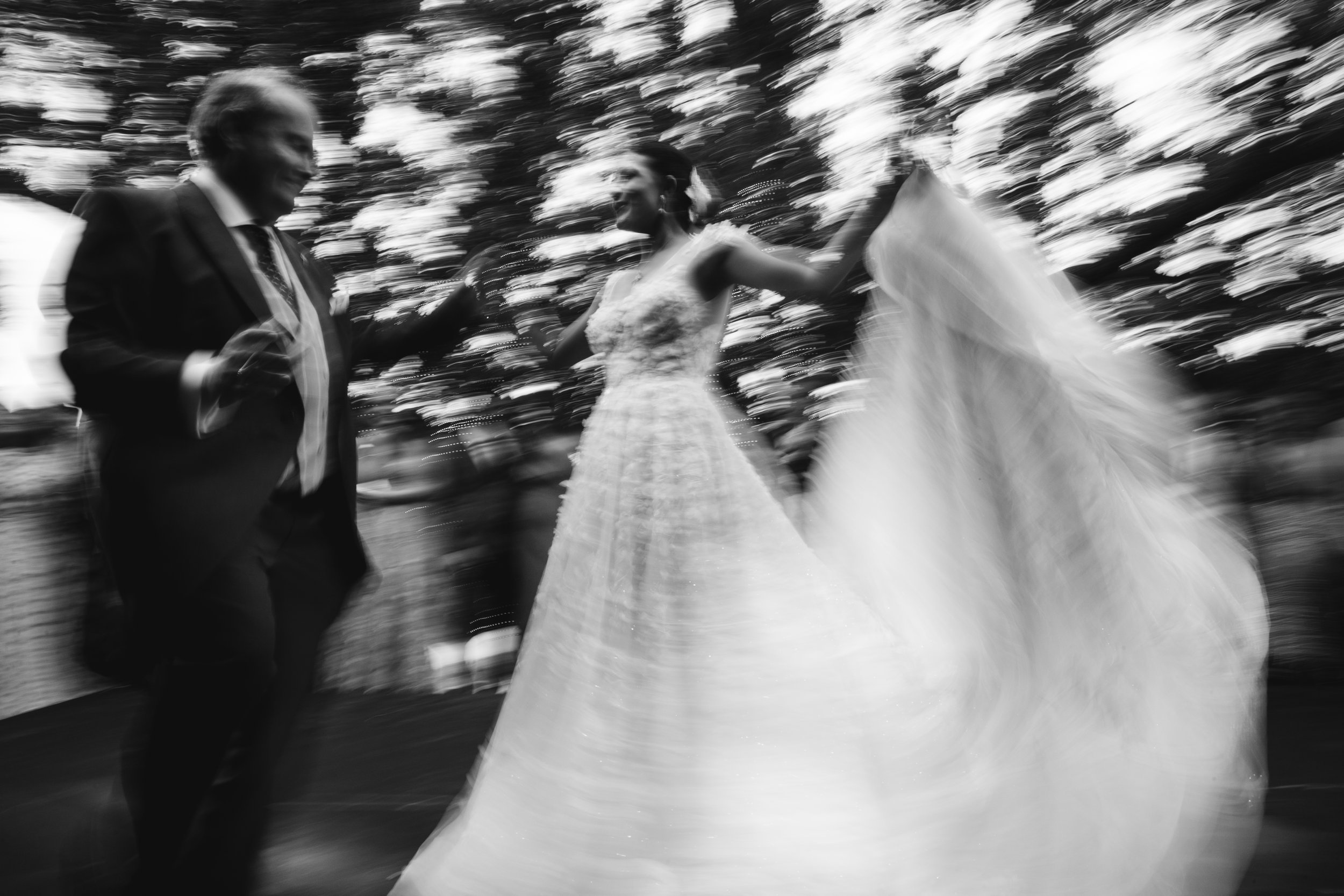 Pareja de boda bailando al aire libre con fondo de árboles, imagen en blanco y negro con efecto de movimiento.