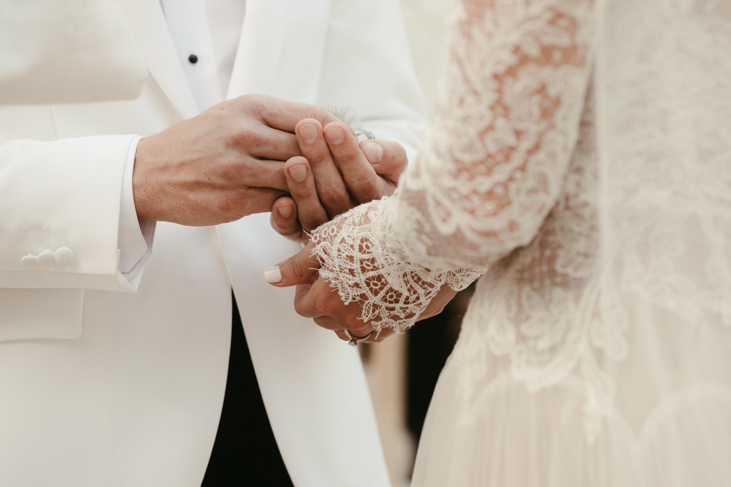 Manos de una pareja de novios tomándose de las manos durante la ceremonia de matrimonio, con detalles en encaje en sus prendas.