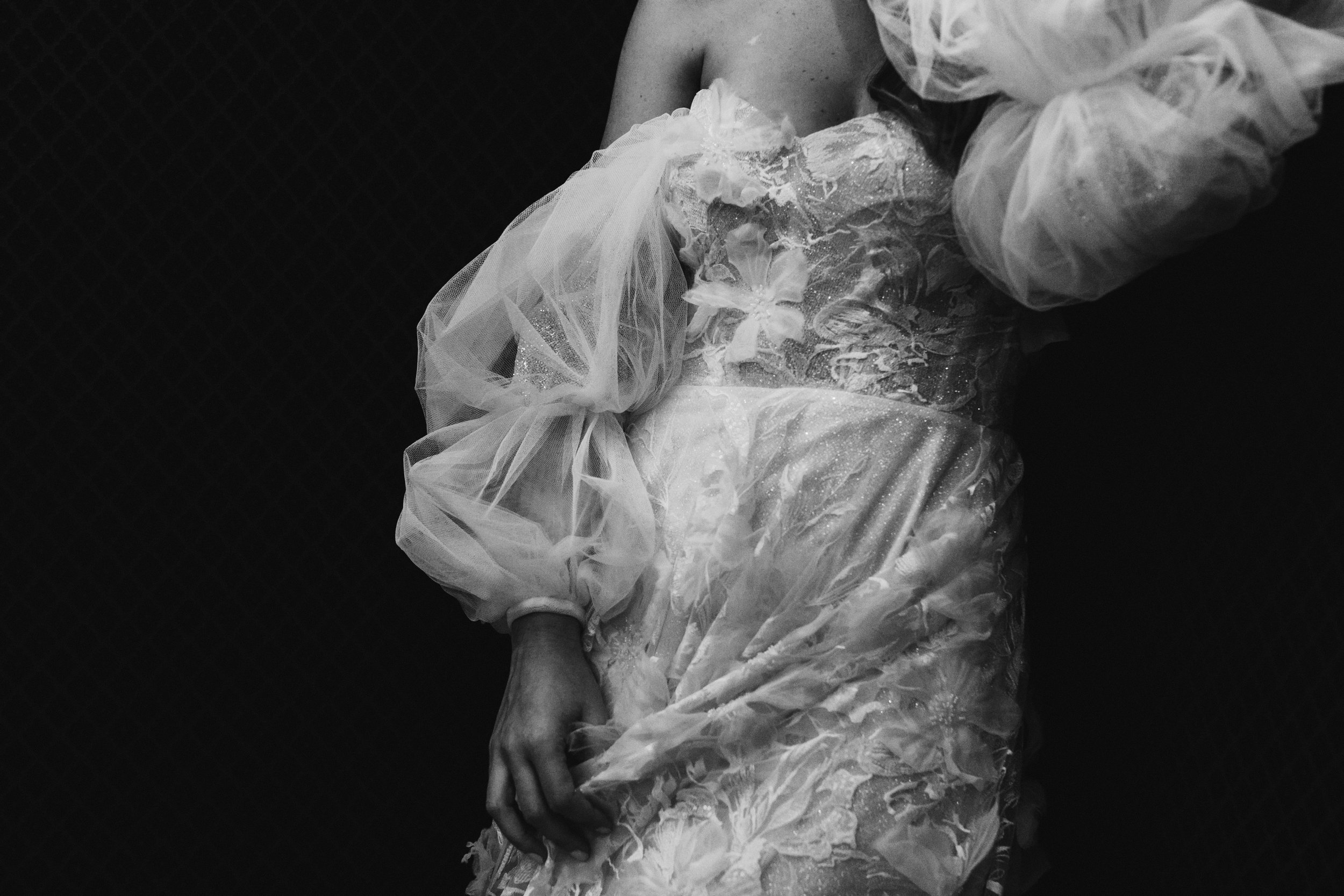 Mujer con vestido de novia blanco y transparente en un fondo oscuro.