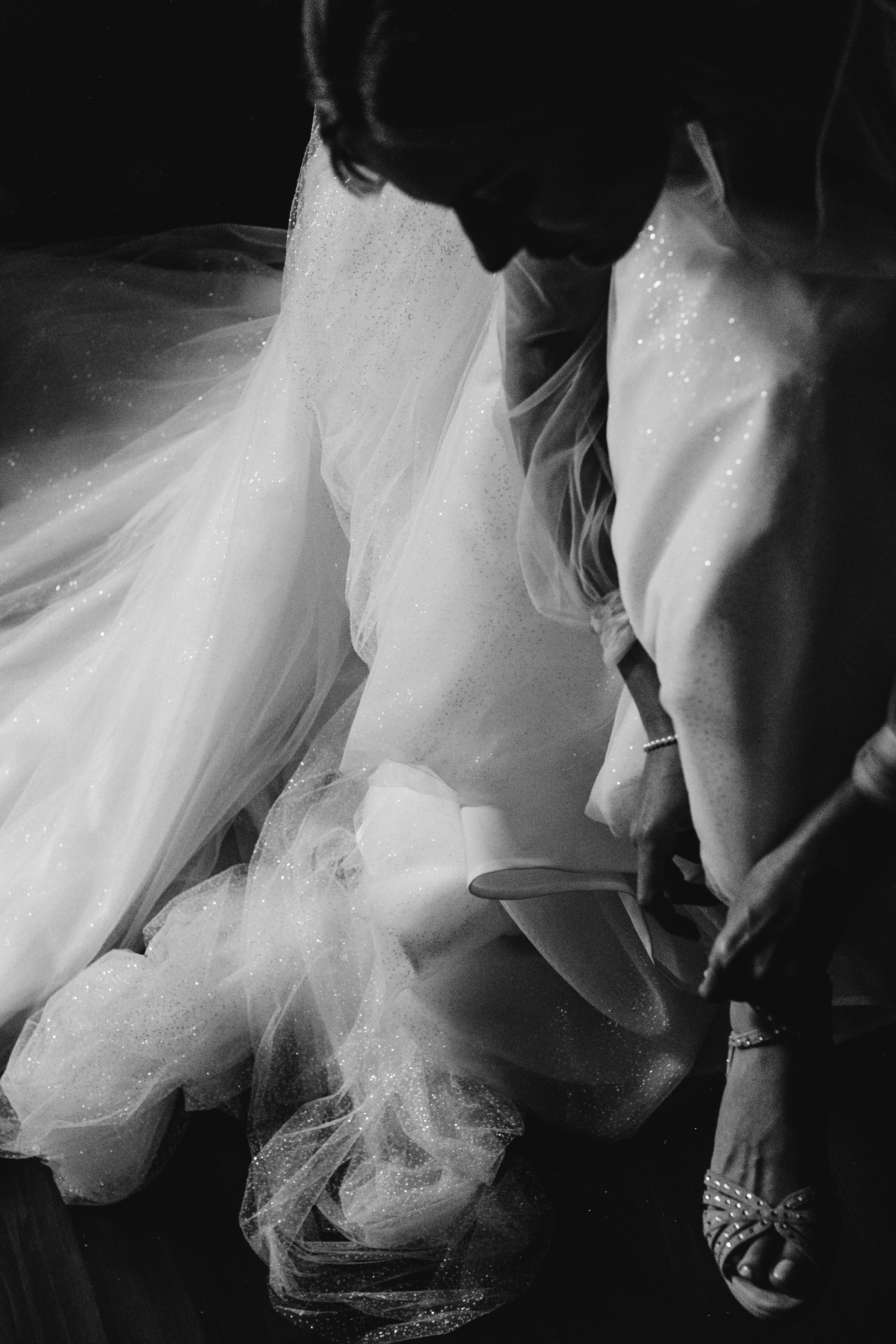 Mujer en vestido de novia ajustándose el zapato, en blanco y negro.