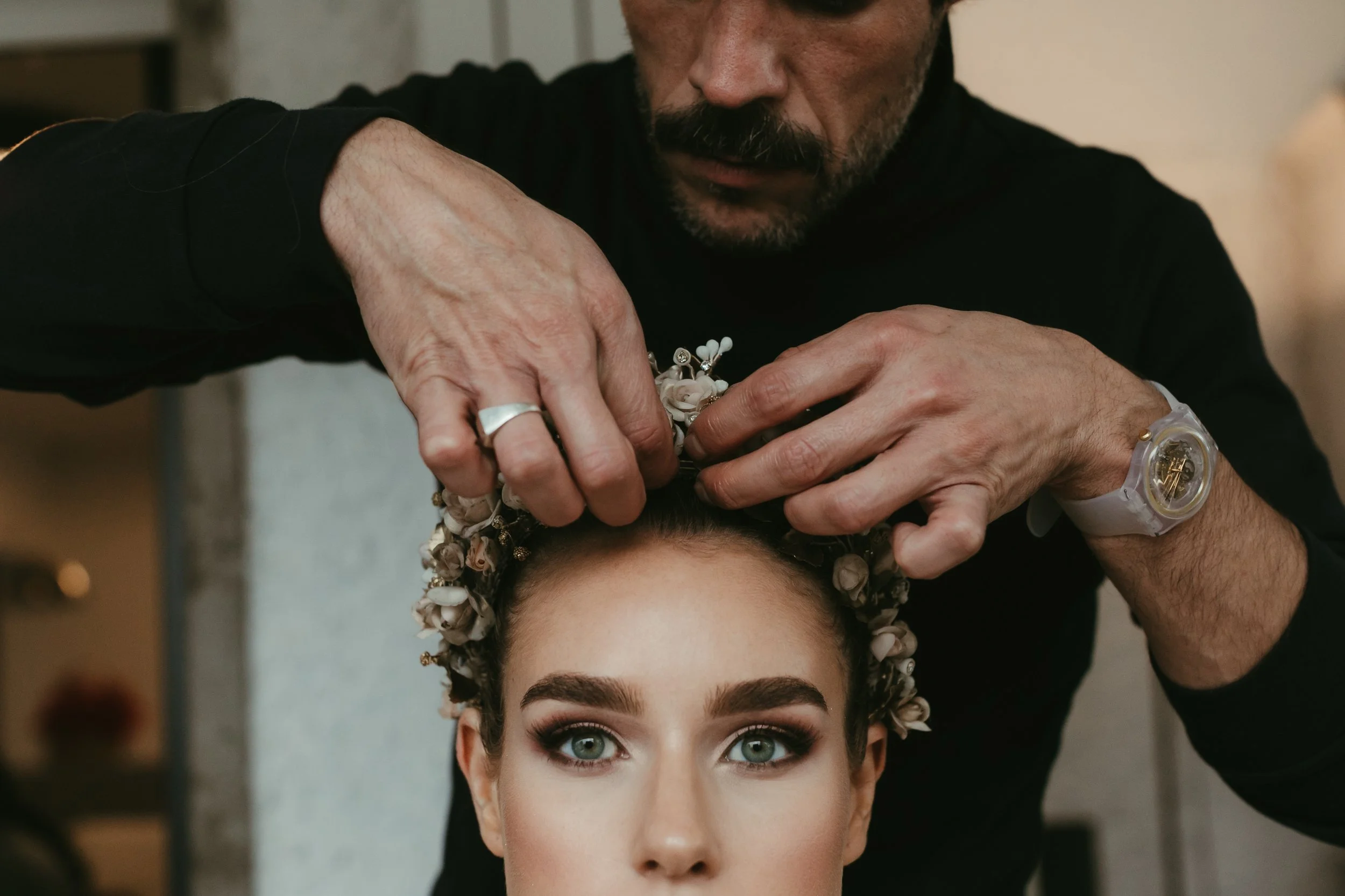 Un hombre colocando una corona de flores en la cabeza de una mujer con ojos azules y maquillaje elaborado.