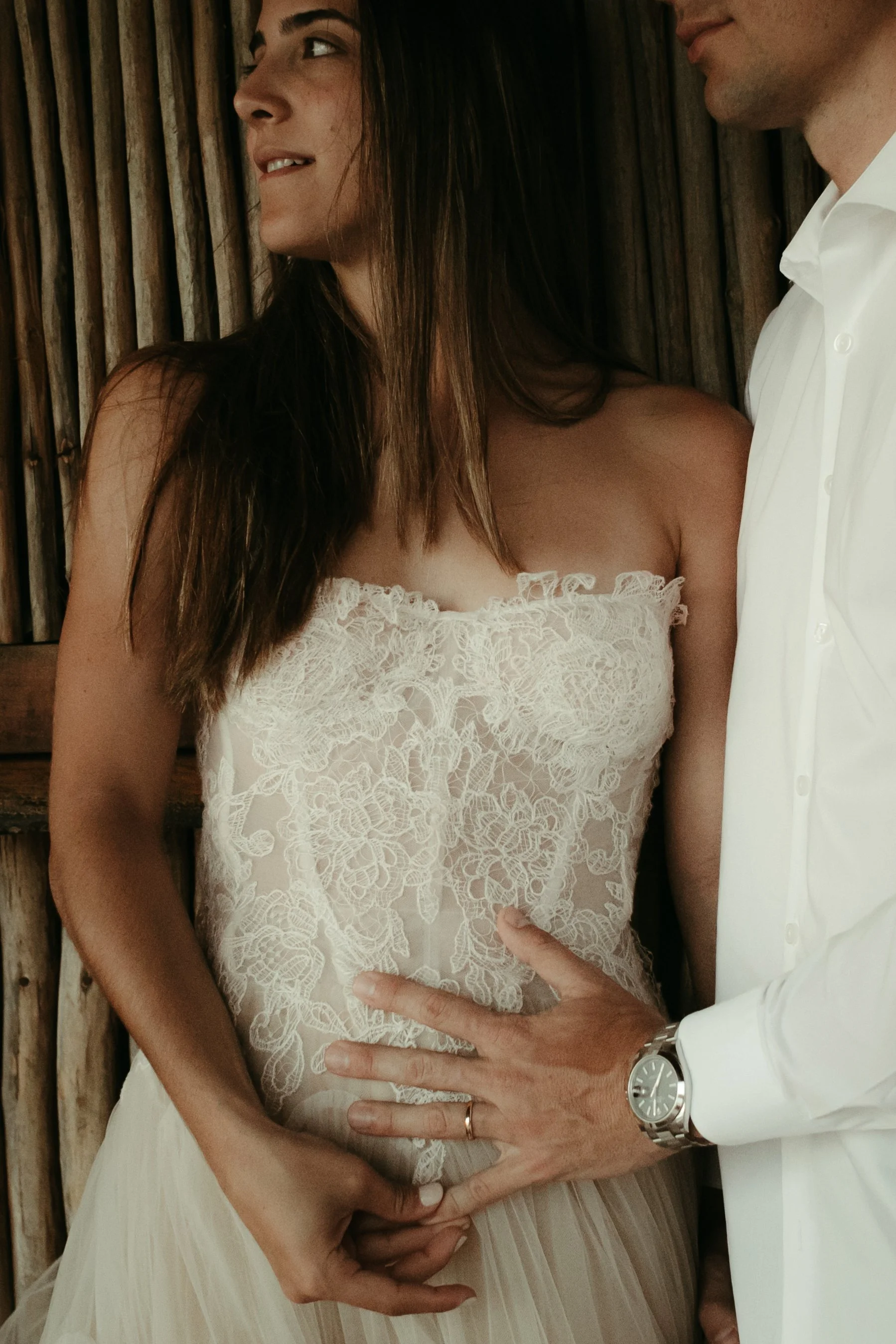 Pareja en una imagen romántica, la mujer viste un vestido de encaje blanco y el hombre lleva una camisa blanca, con la mano del hombre en la cintura de la mujer.