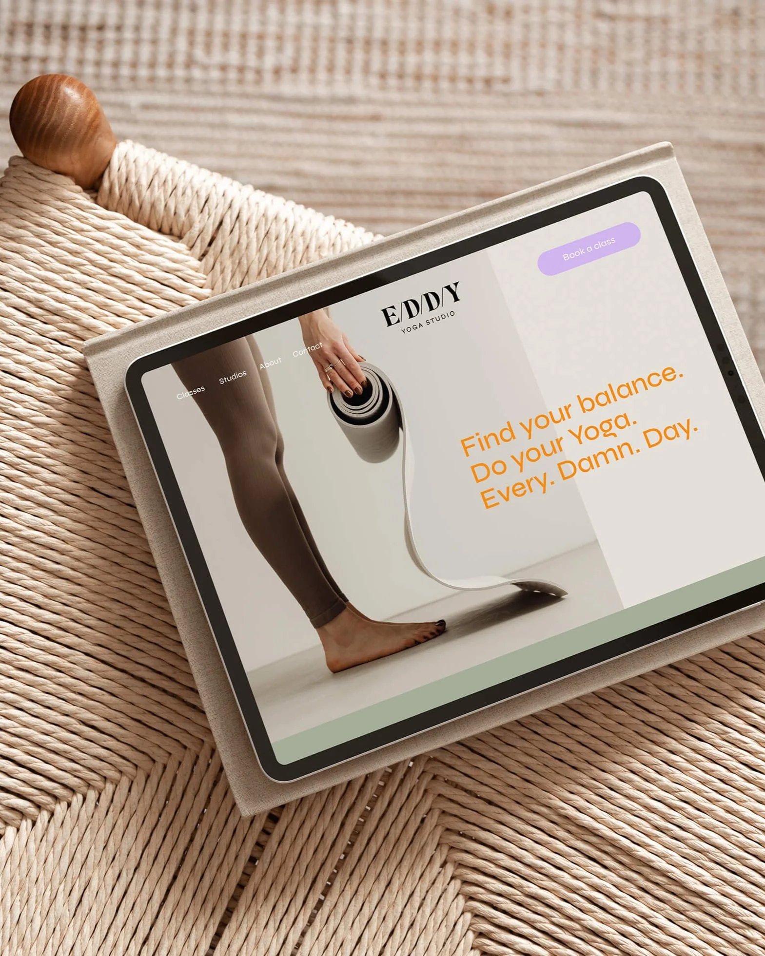 Tablet auf einem geflochtenen Sitz mit einer Website für ein Yoga-Studio, zeigt ein Person, die eine Yogamatte rollt.