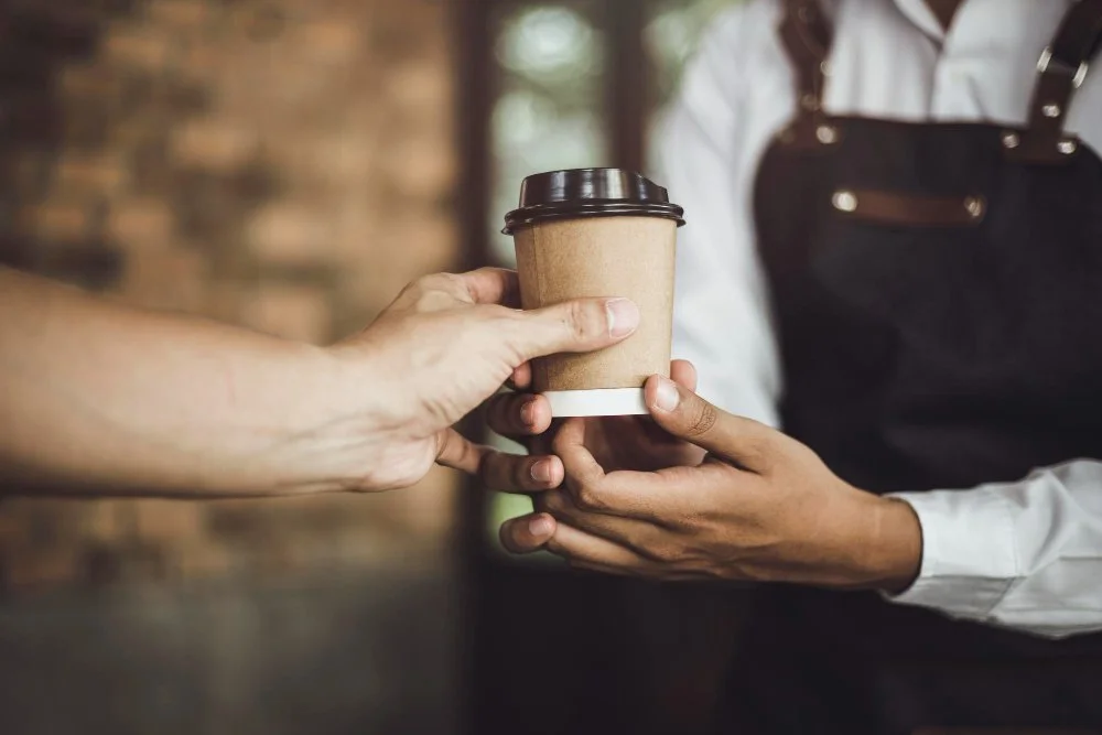 Person receiving a disposable coffee cup from another person at a coffee shop.