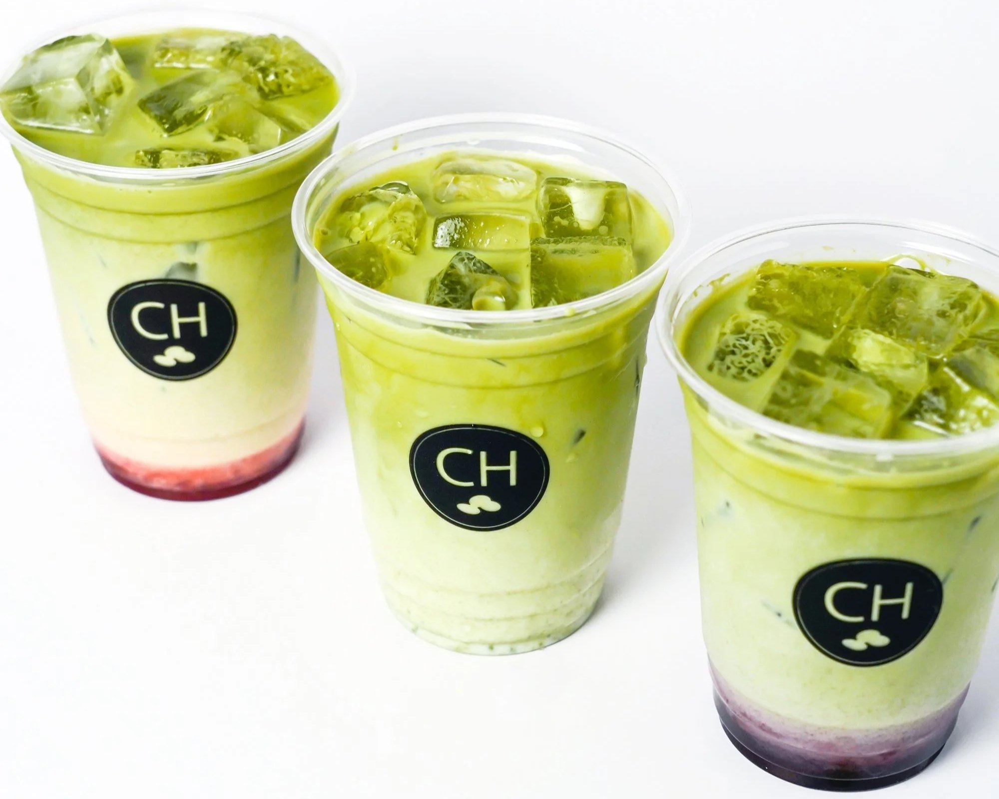 Three coffee house cups lined up with iced matcha drinks in strawberry, original, and blueberry flavours