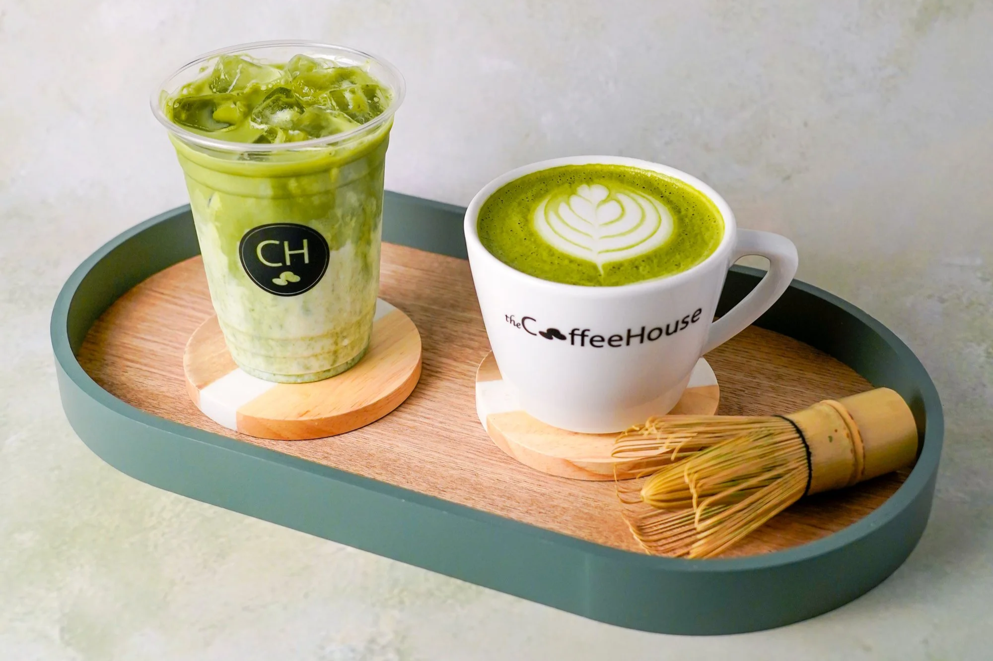 An iced matcha and a hot matcha on a café table, with a traditional bamboo matcha whisk