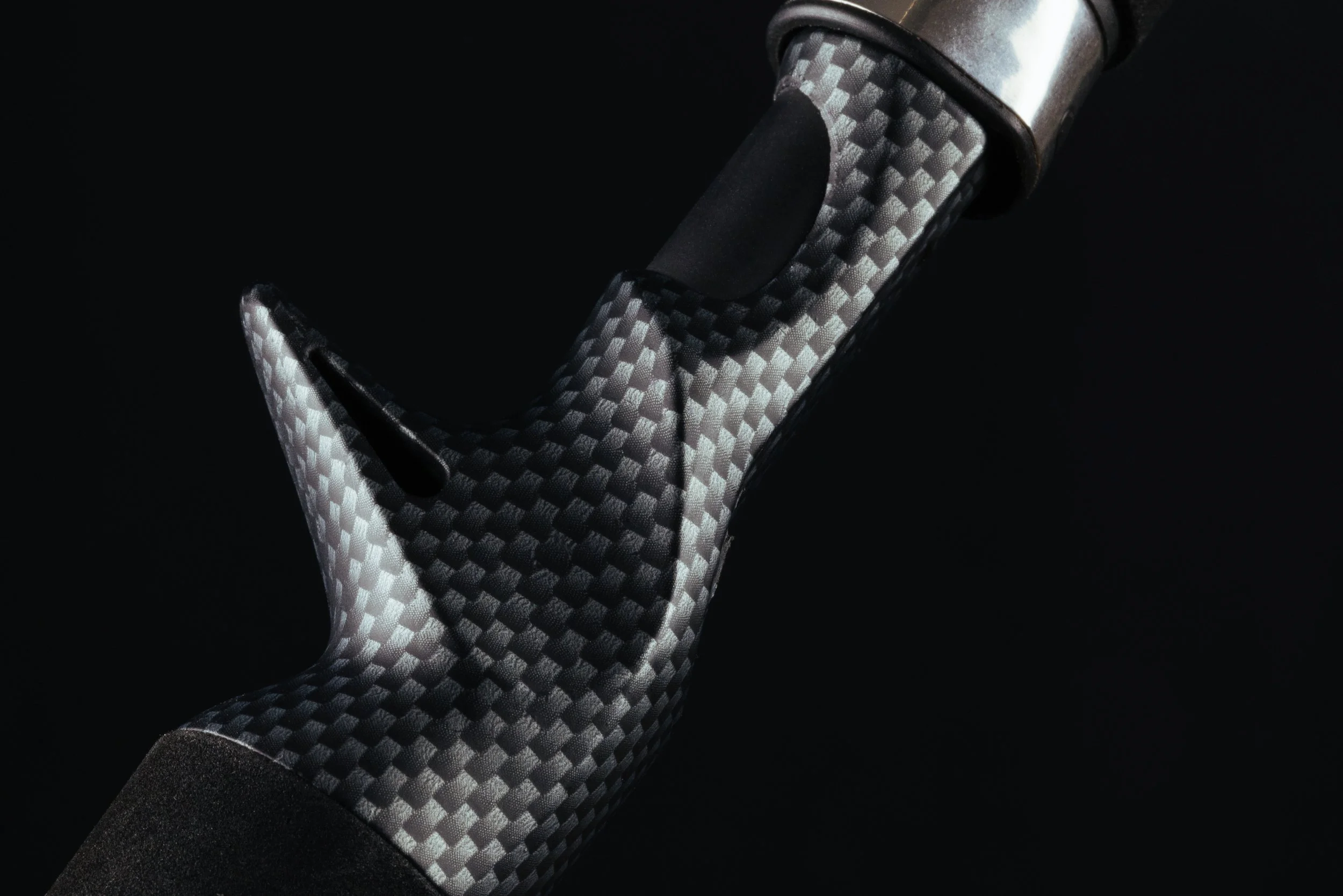 Close-up of a golf club with a carbon fiber pattern grip on a black background.