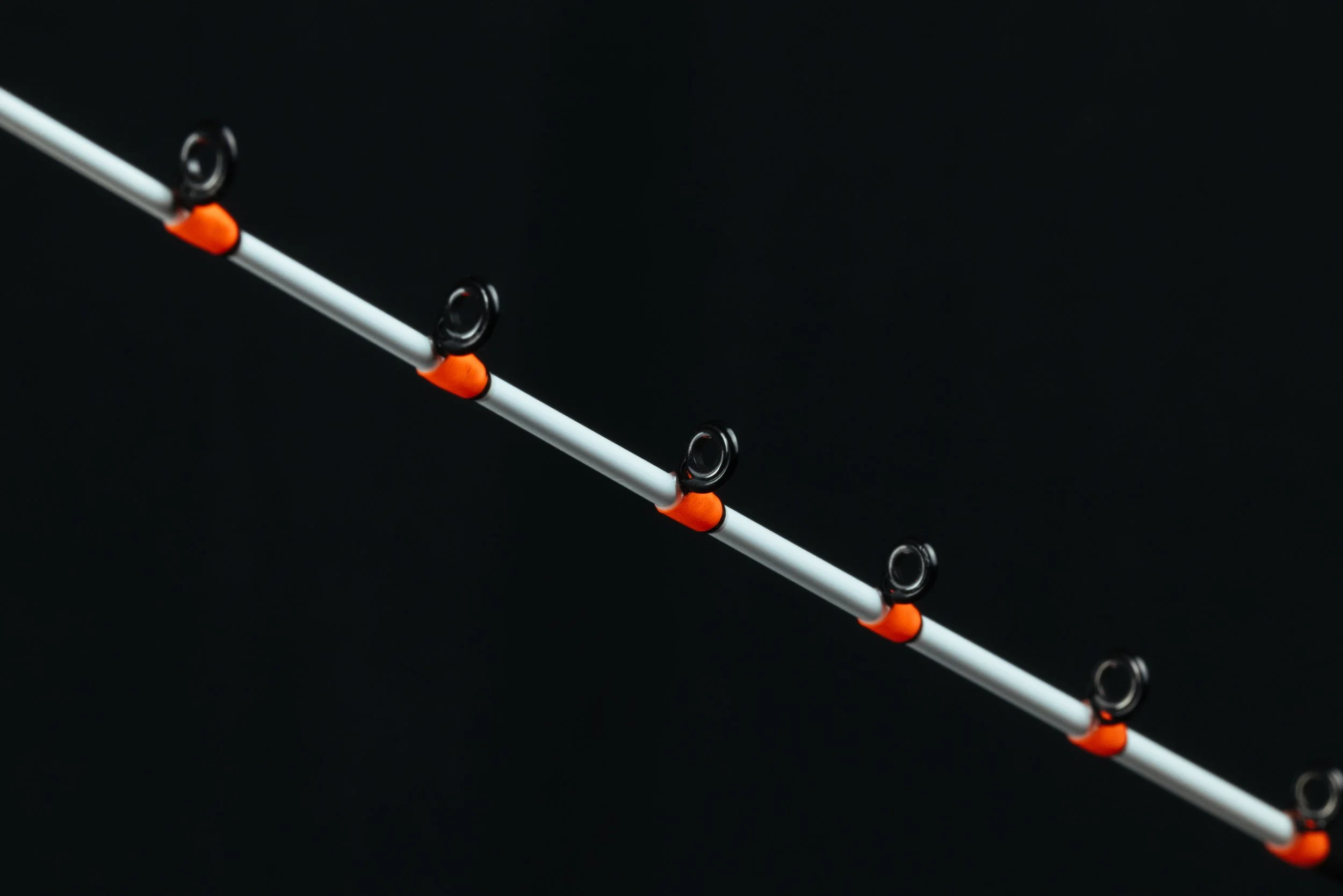 Fishing rod with multiple black eyelets and orange connectors against a black background.