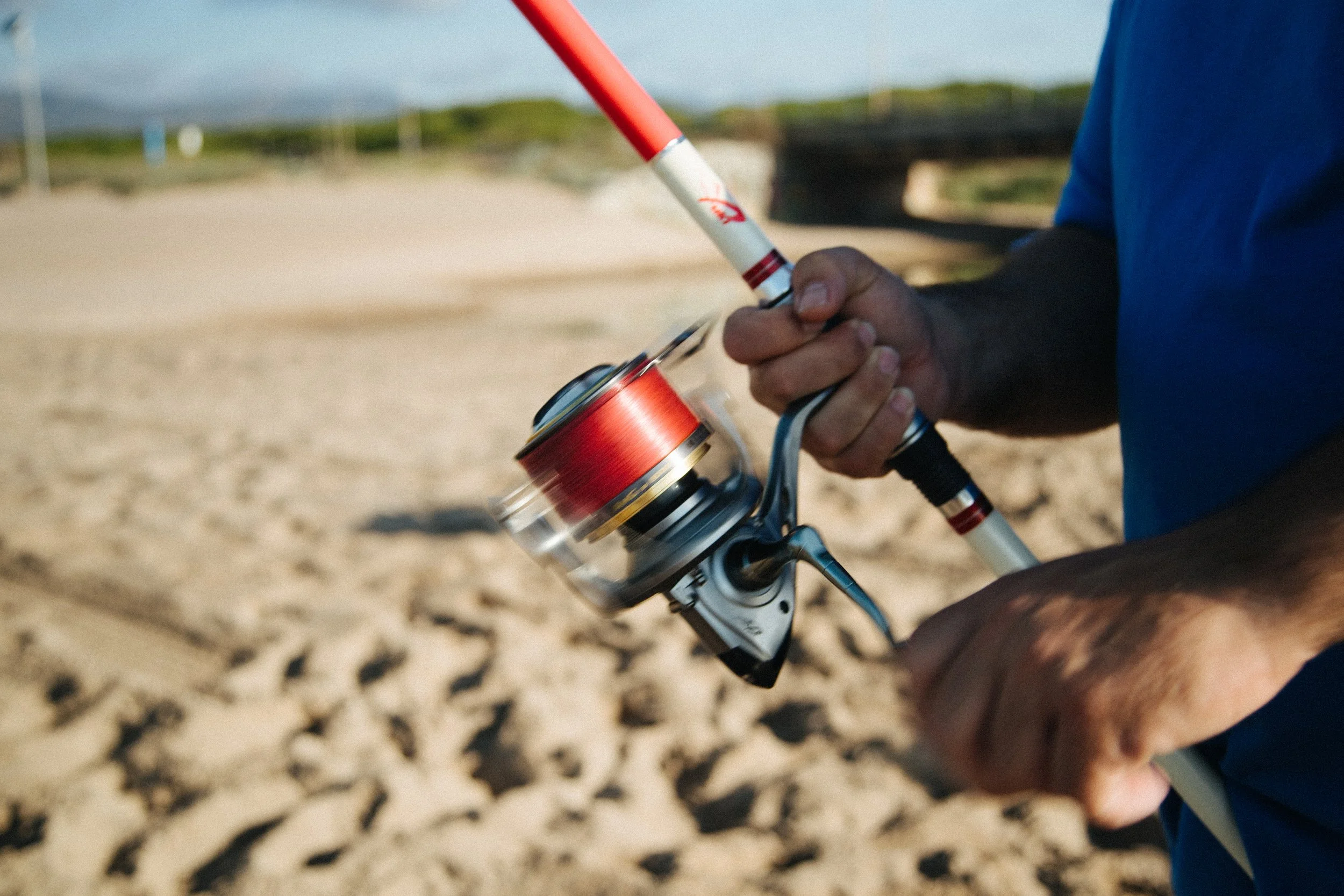 Close-up of a person holding a fishing rod with a reel, standing on a sandy beach.