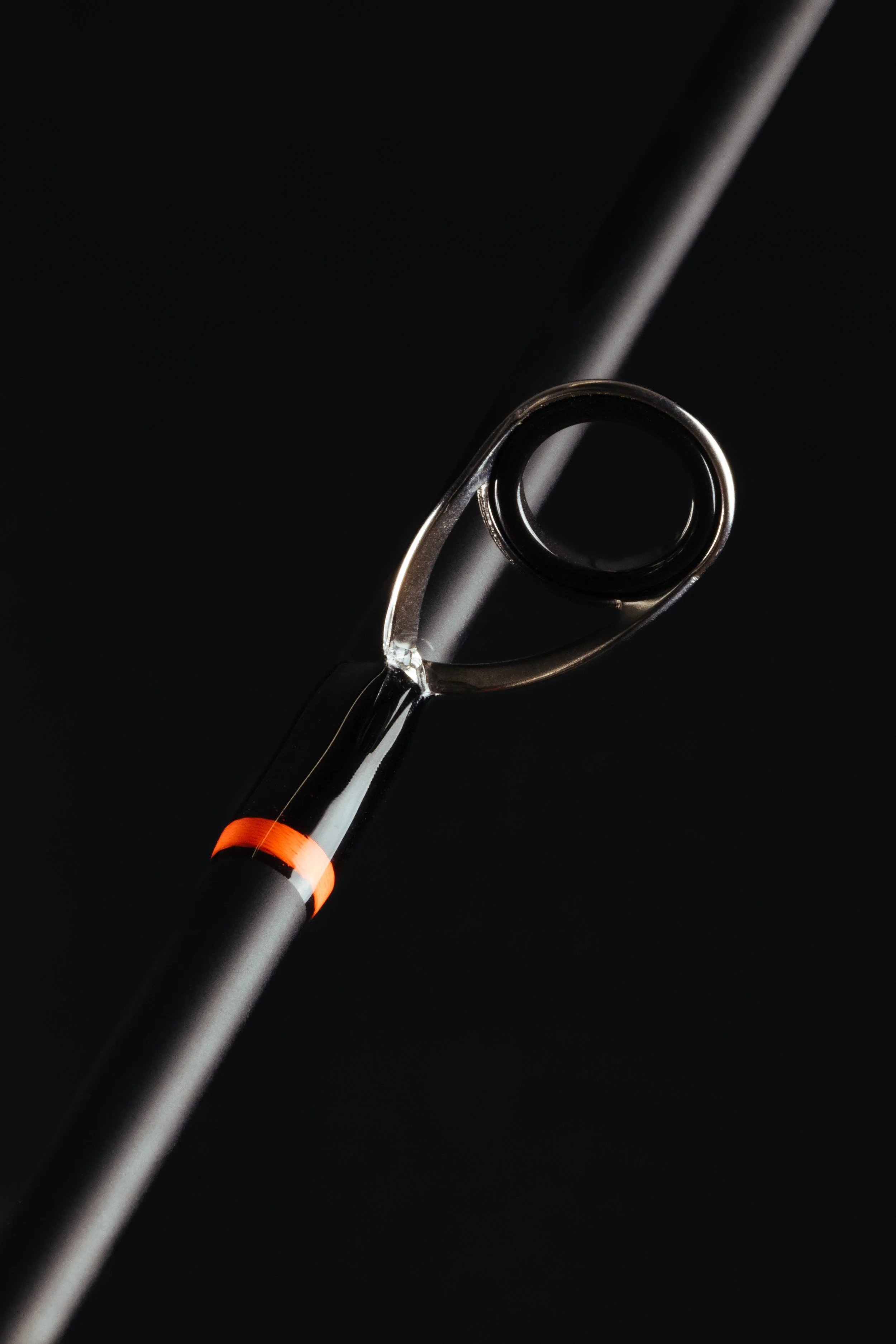 Close-up of a fishing rod eyelet with a guiding line passing through, against a black background.