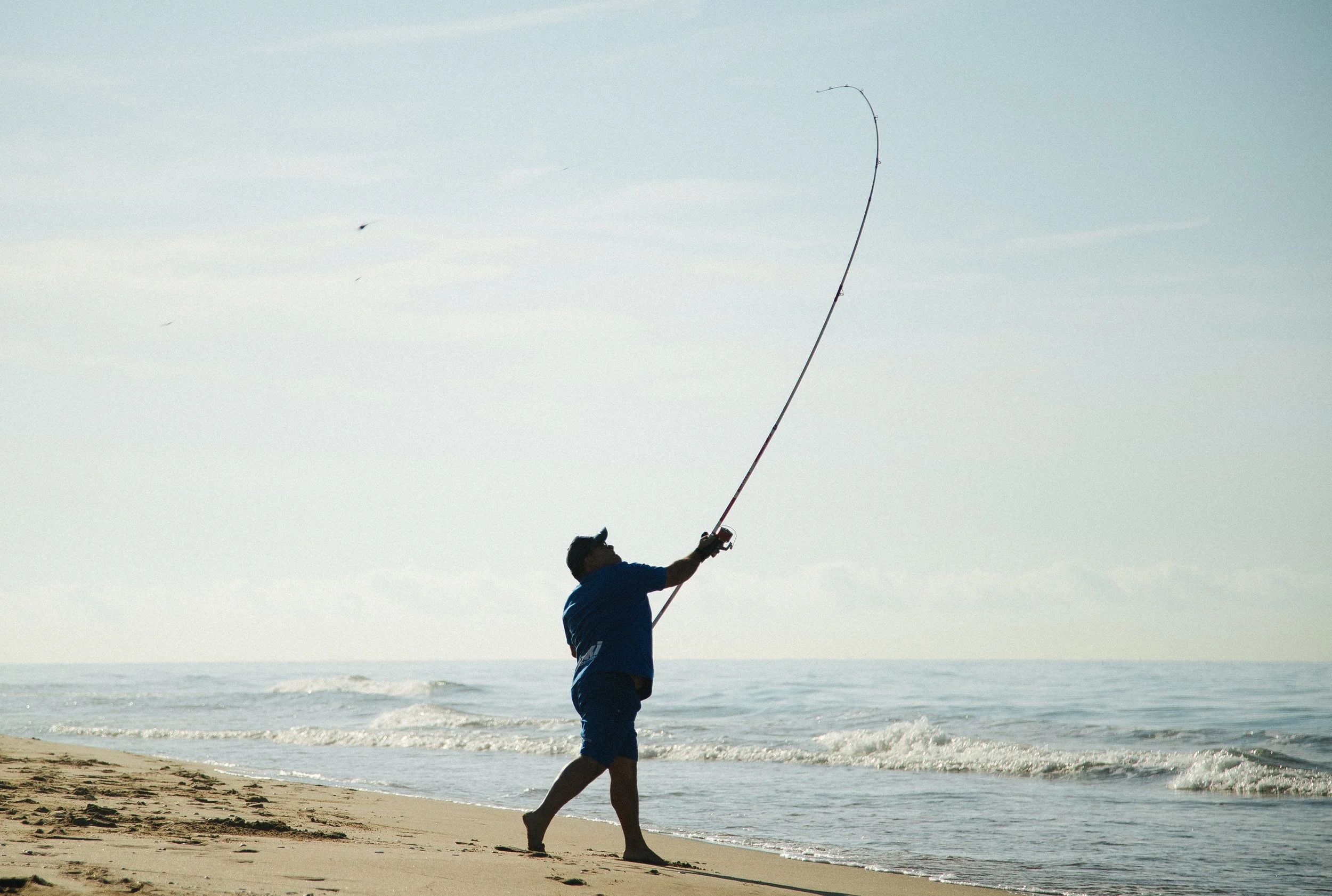 Person fishing on the beach with an overhead fishing rod in the air