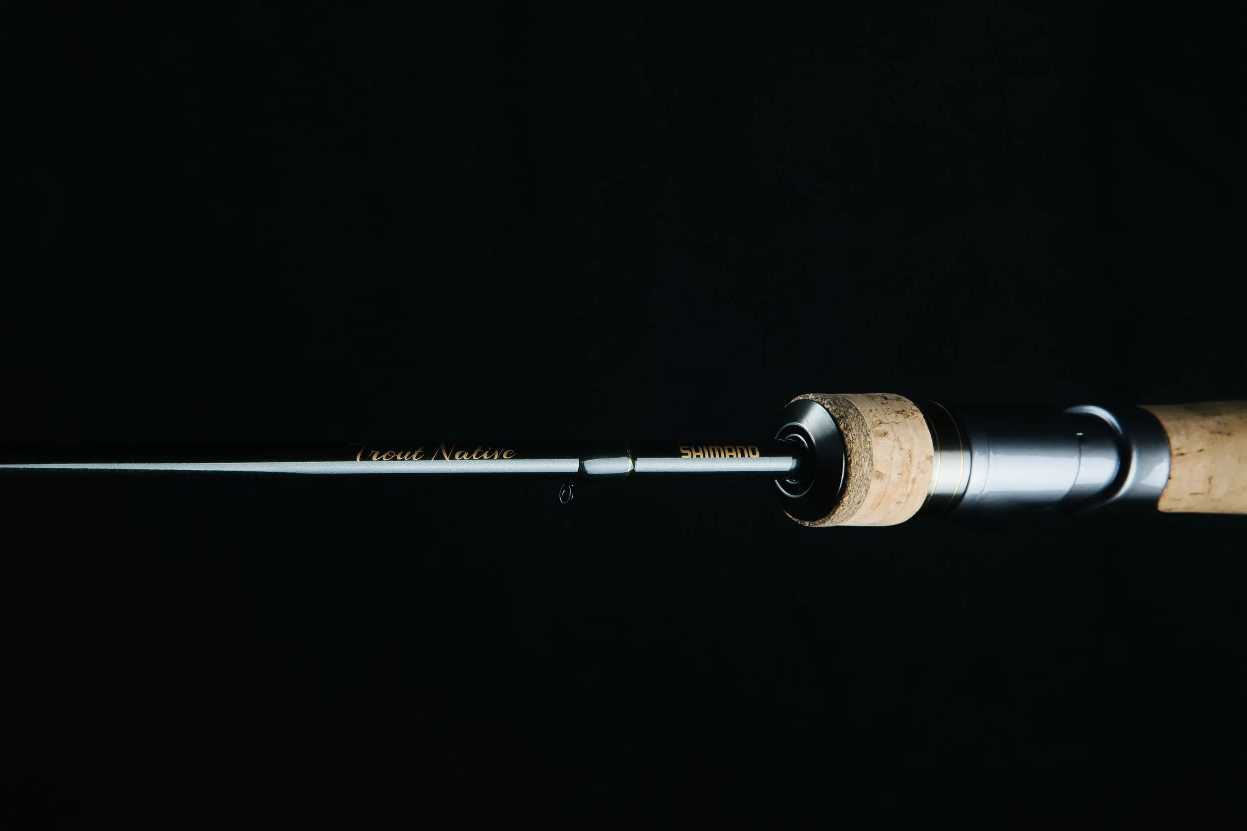 Close-up of a fishing rod with a cork handle against a black background.
