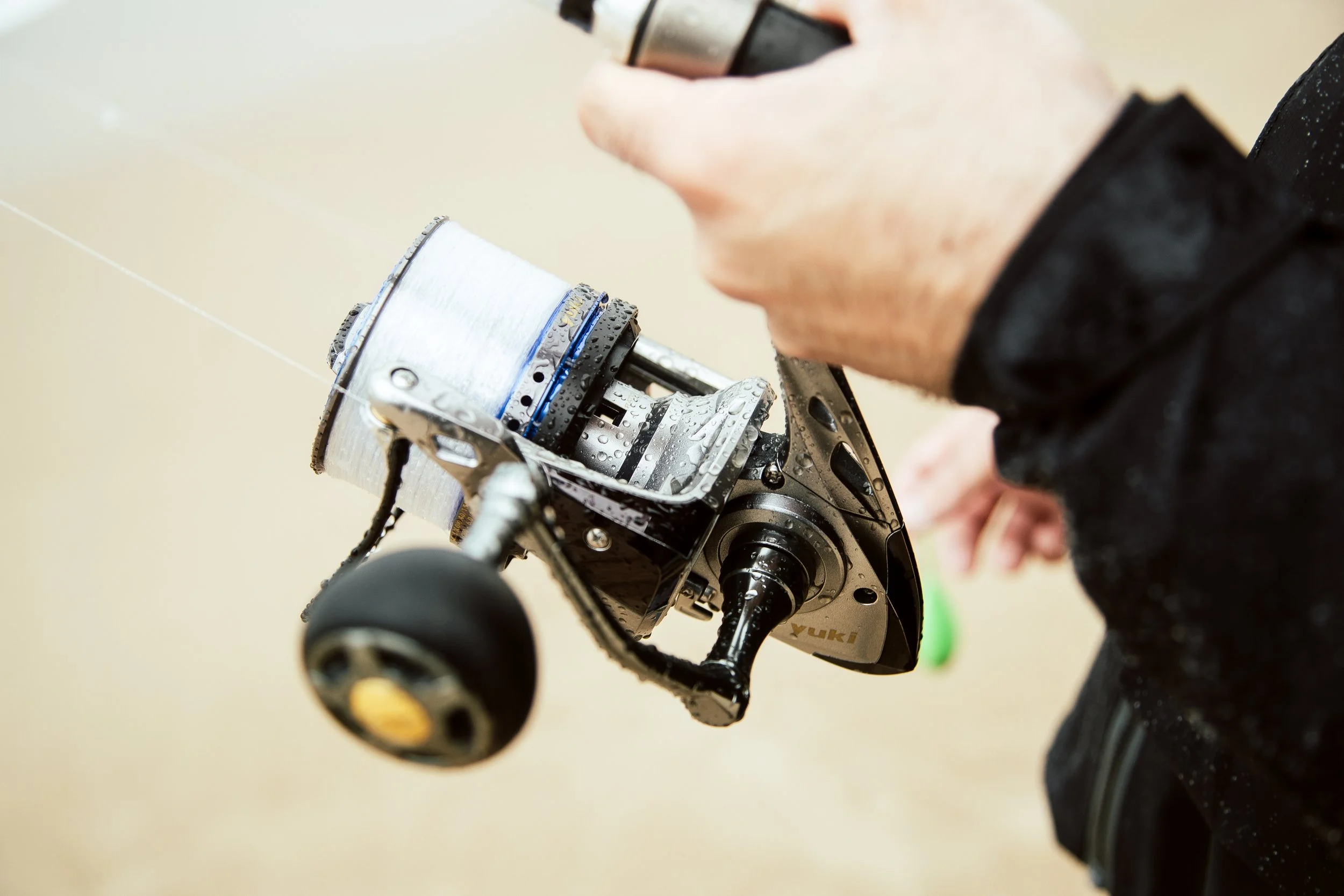 Person holding a fishing reel with water droplets, focusing on the reel's details.