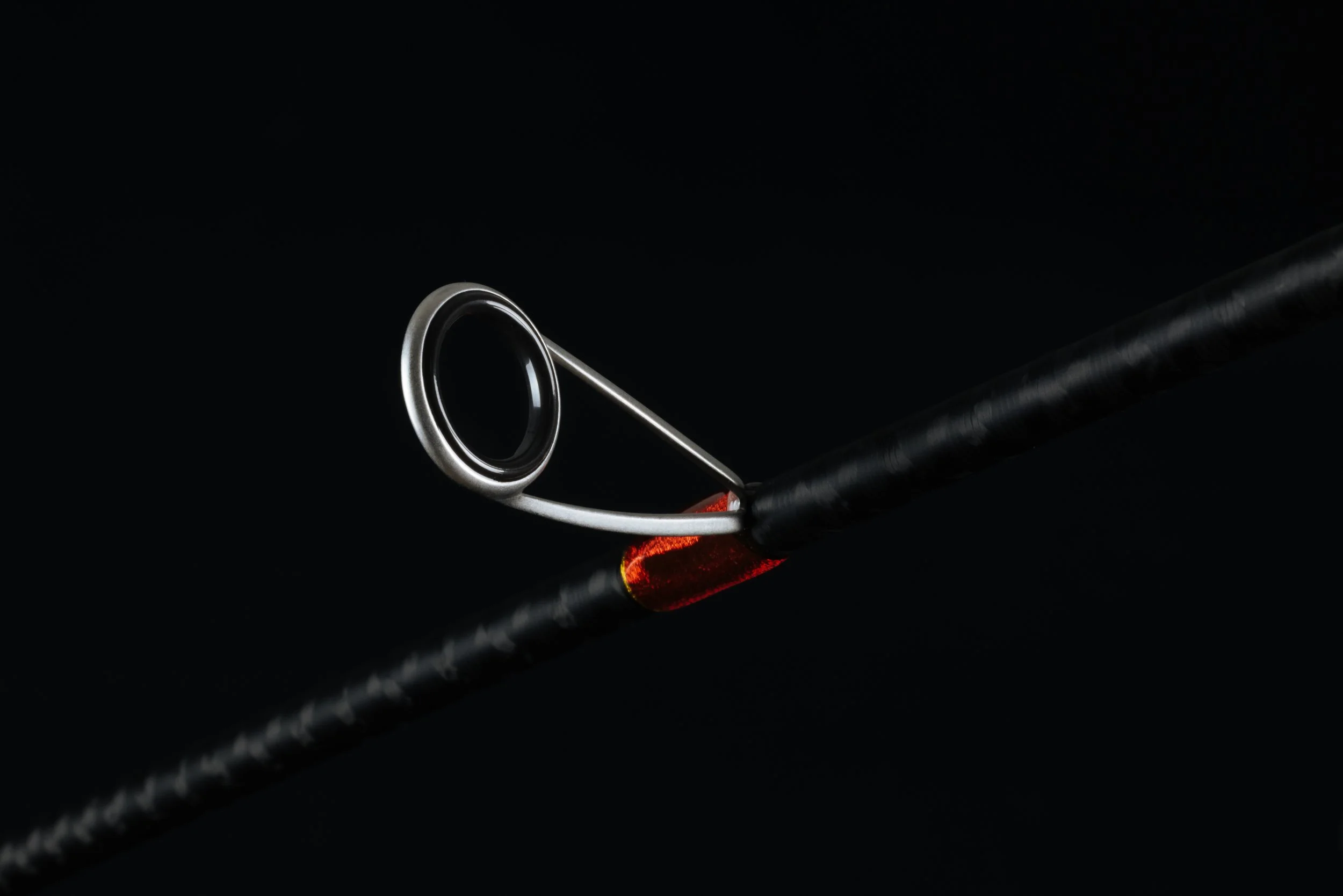Close-up of a fishing hook embedded in a fishing rod's eyelet with glowing red light underneath on a black background.