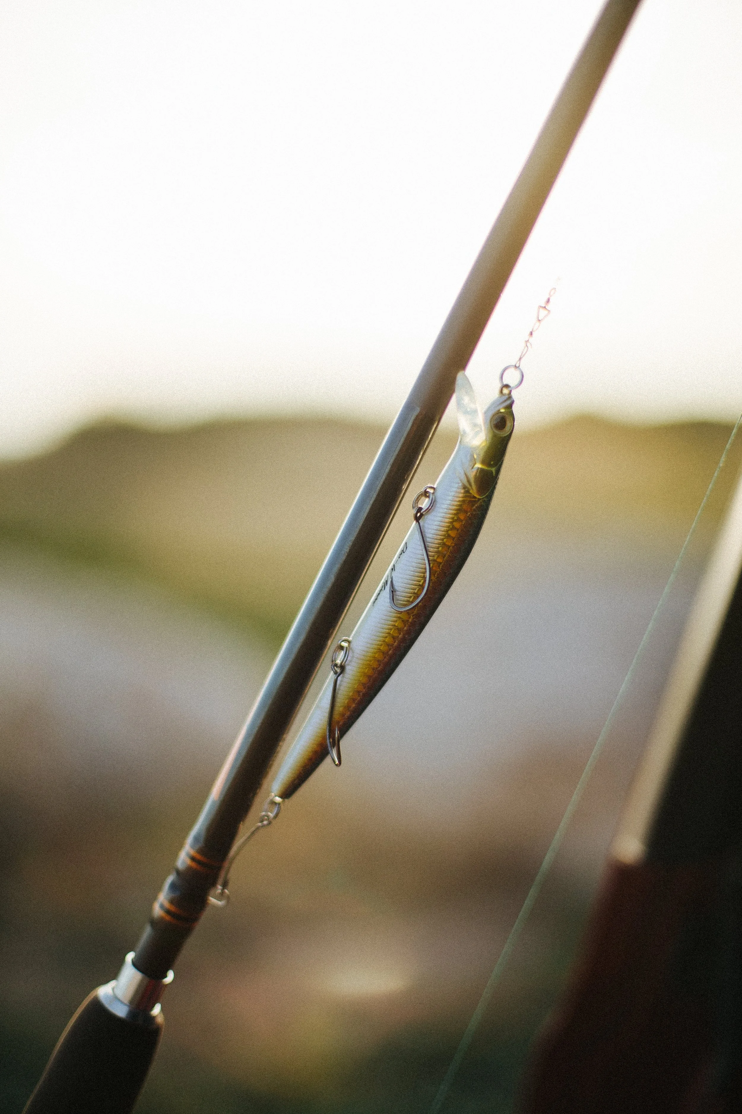 Fishing rod with a lure hanging from the line outdoors with blurred background