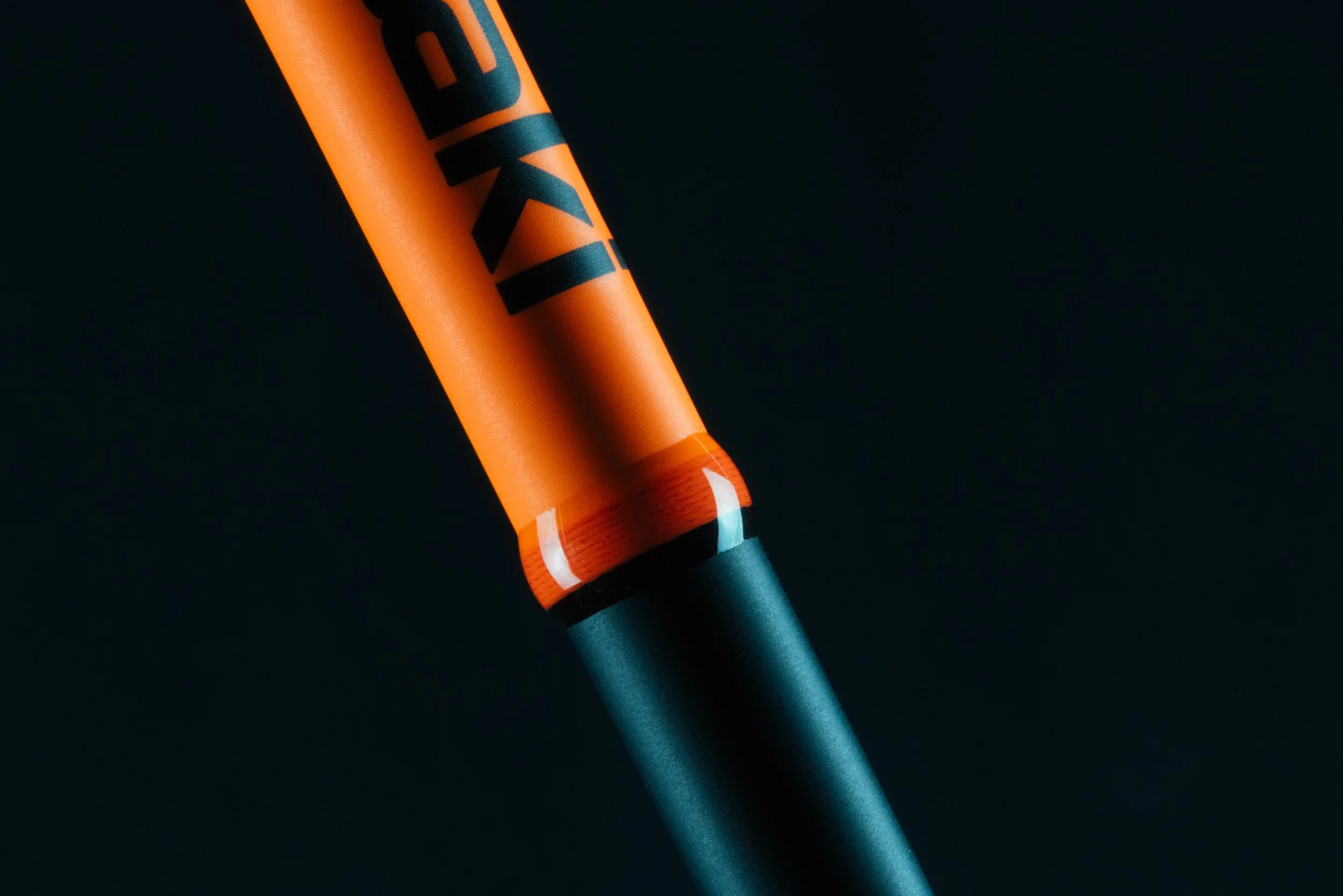 Close-up of a black baseball bat with an orange handle and black lettering on a dark background.