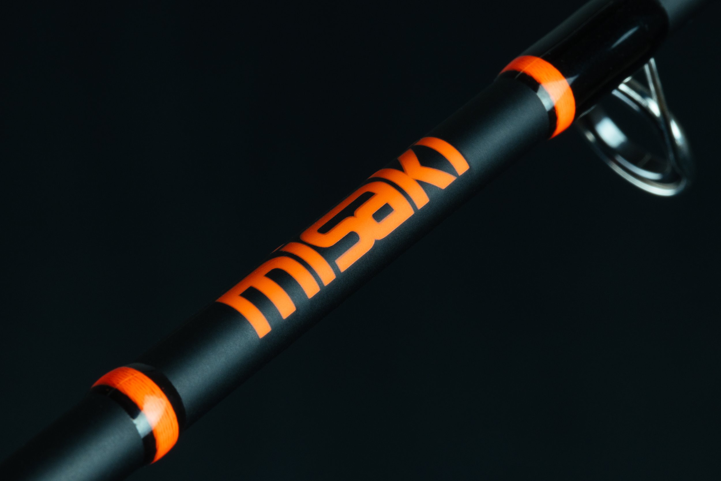 Close-up of a black fishing rod with orange accents and the word "MASSIVE" written on it, against a dark background.