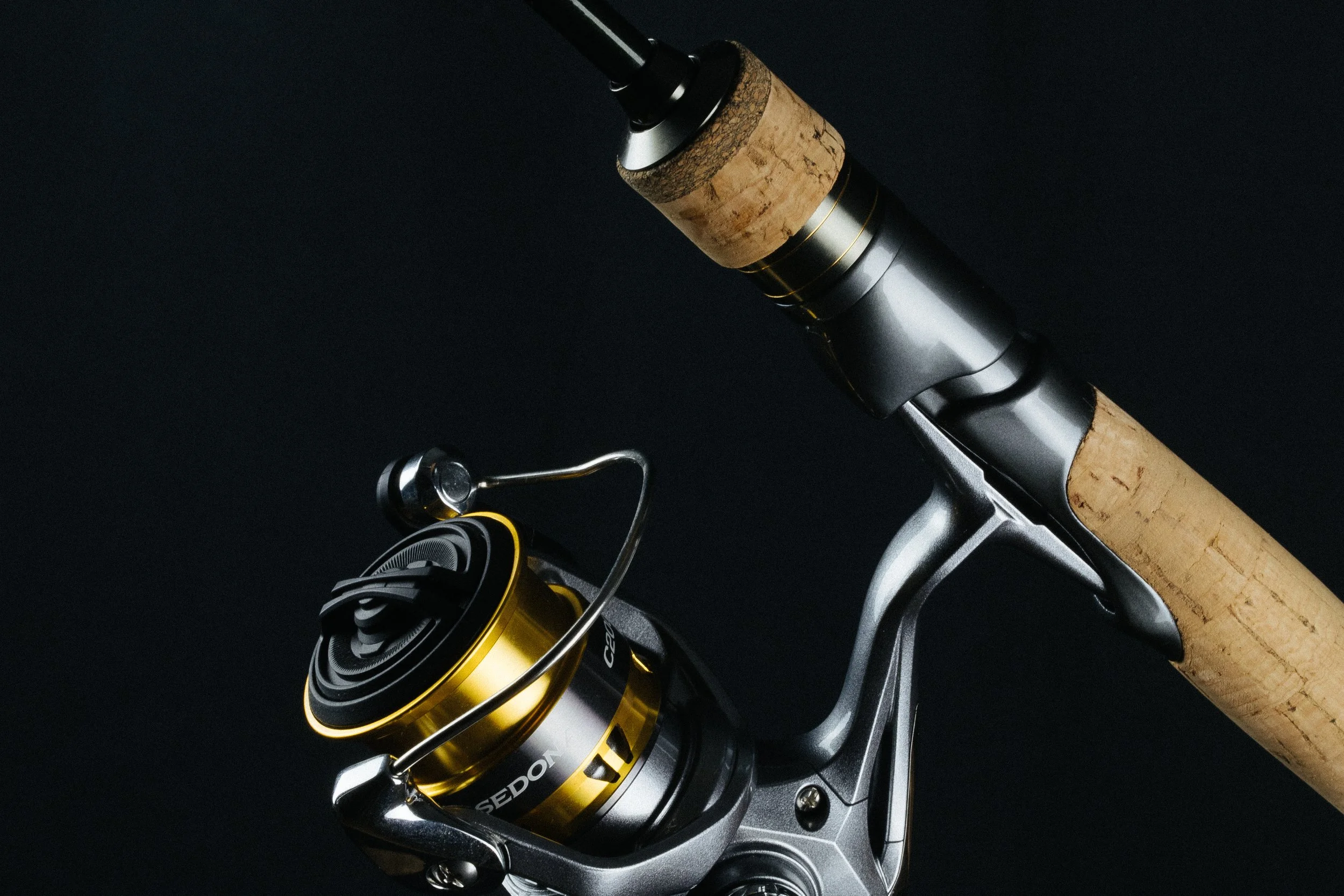 Close-up of a fishing rod with a black and gold spinning reel against a dark background.
