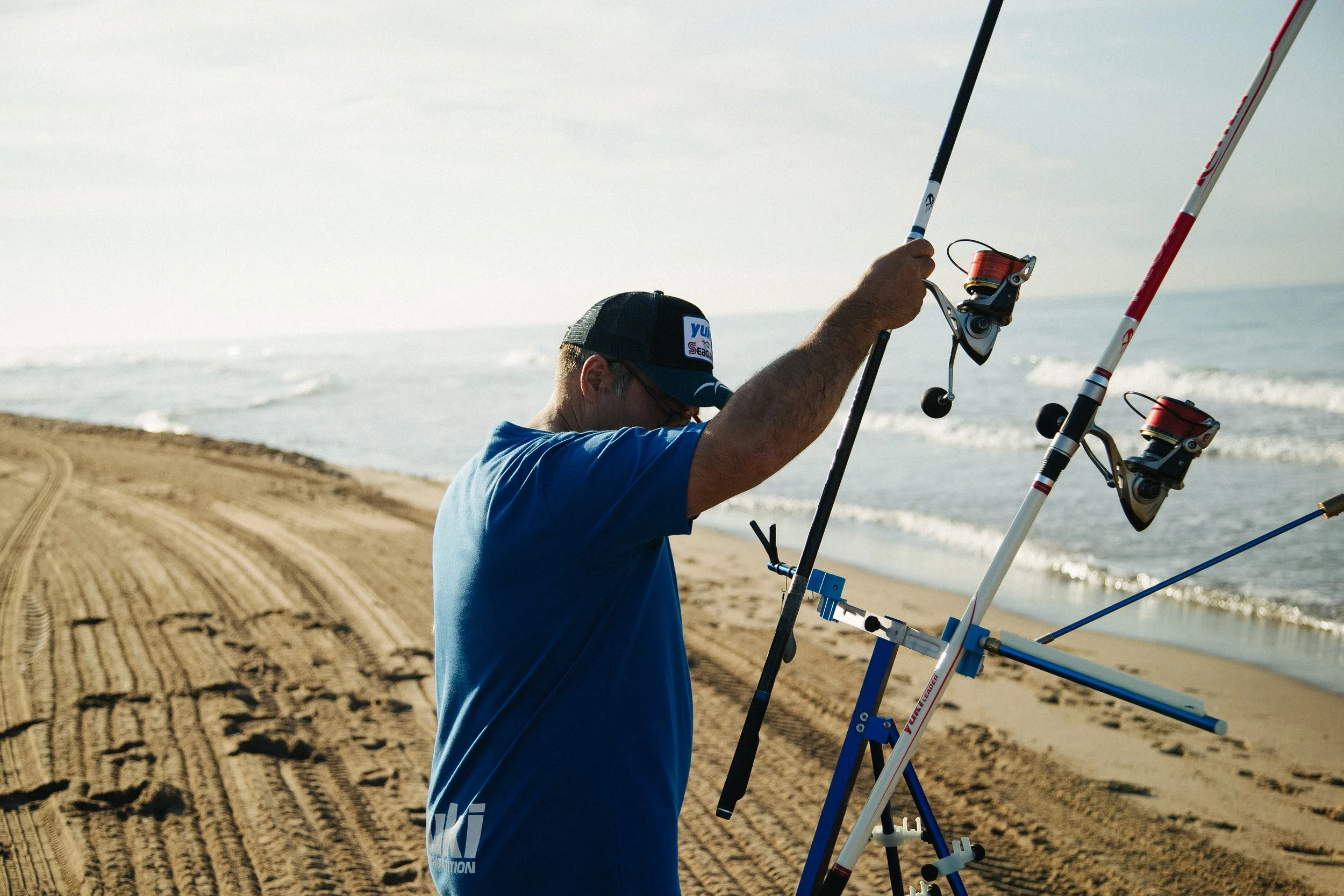 A man setting up fishing rods on a sandy beach near the ocean during daylight.