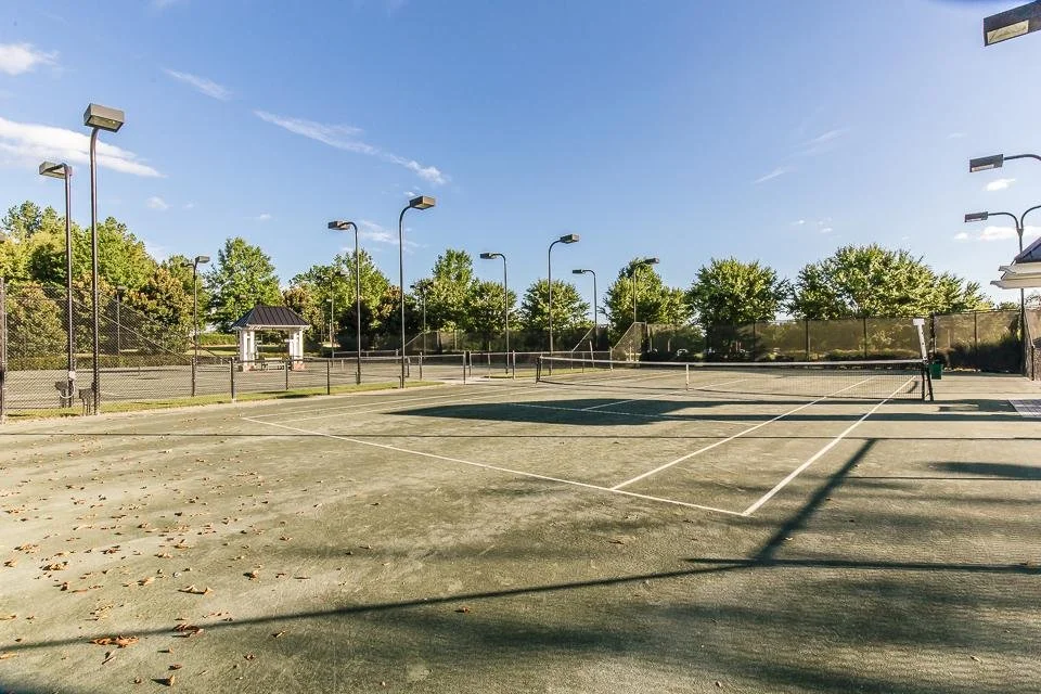 The Georgia Club outdoor tennis court with trees and a small pavilion in the background, under a clear blue sky.