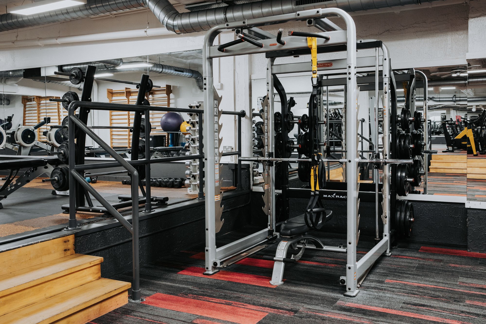 Empty gym with black workout machines and red-black patterned carpet.