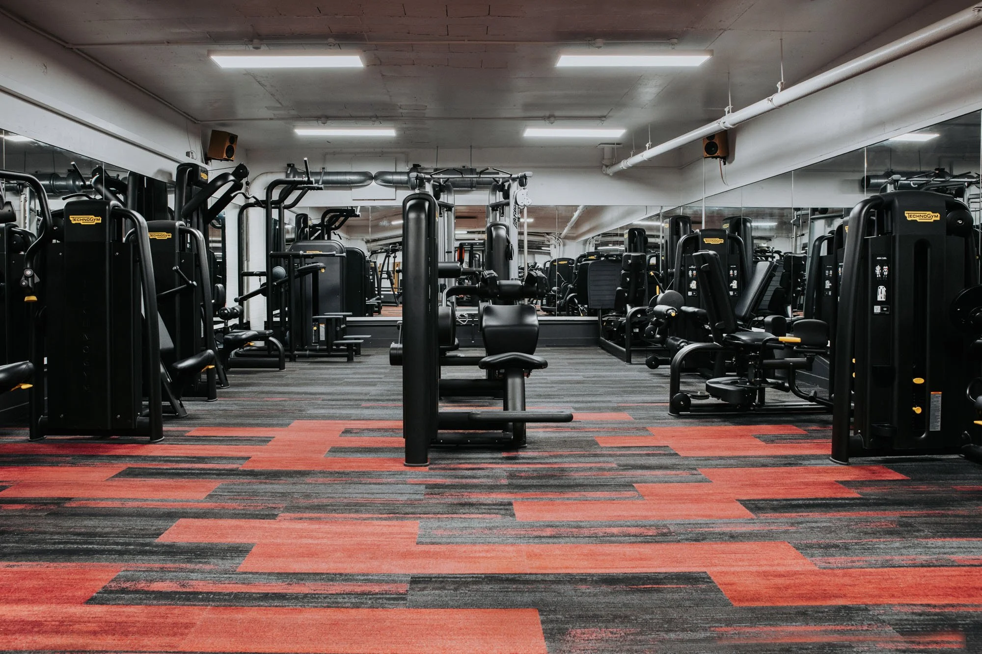 Empty gym with black workout machines and red-black patterned carpet.