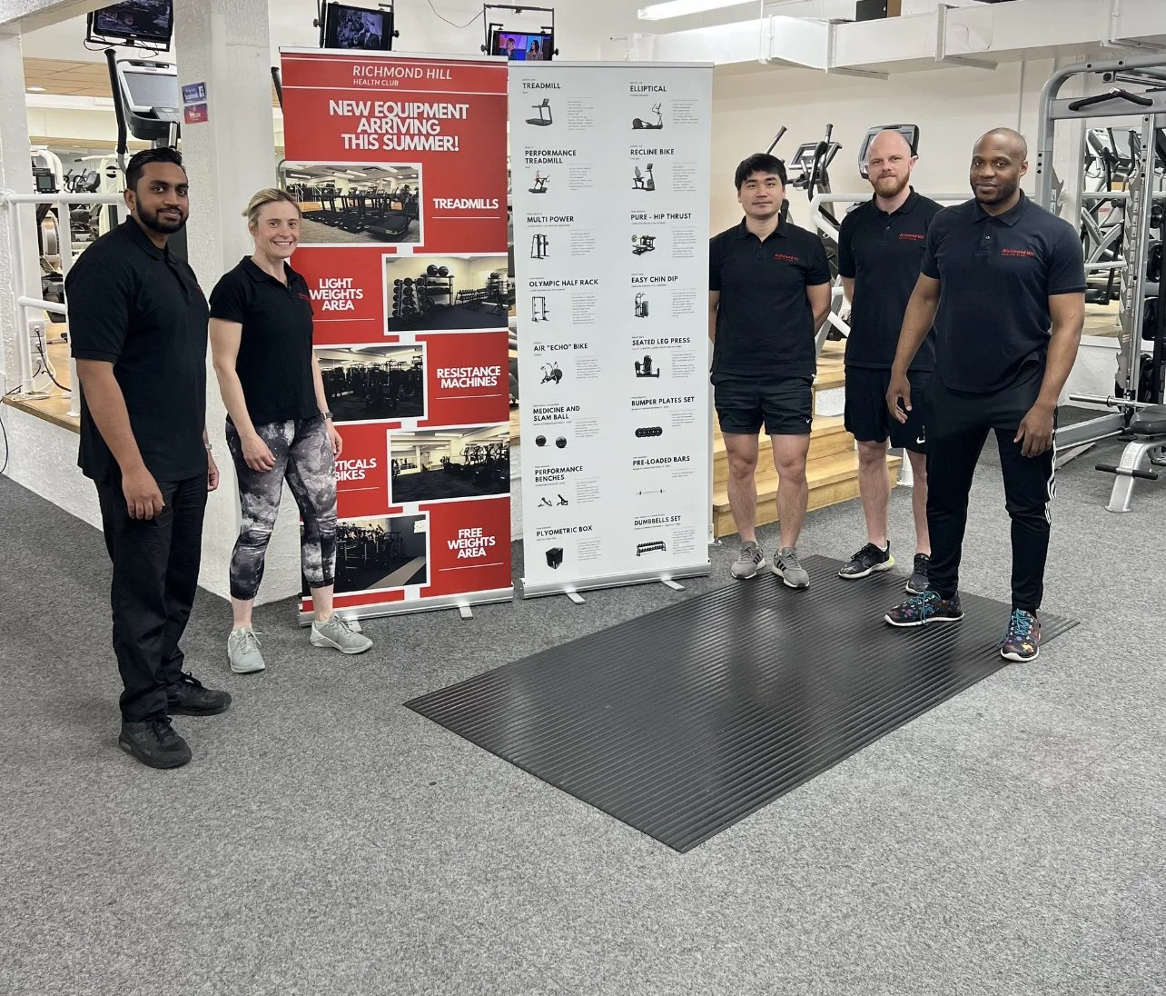 Five people standing in a gym next to a sign with new gym equipment at Richmond Hill Health Club, including treadmills, light weights, resistance machines, and bikes.