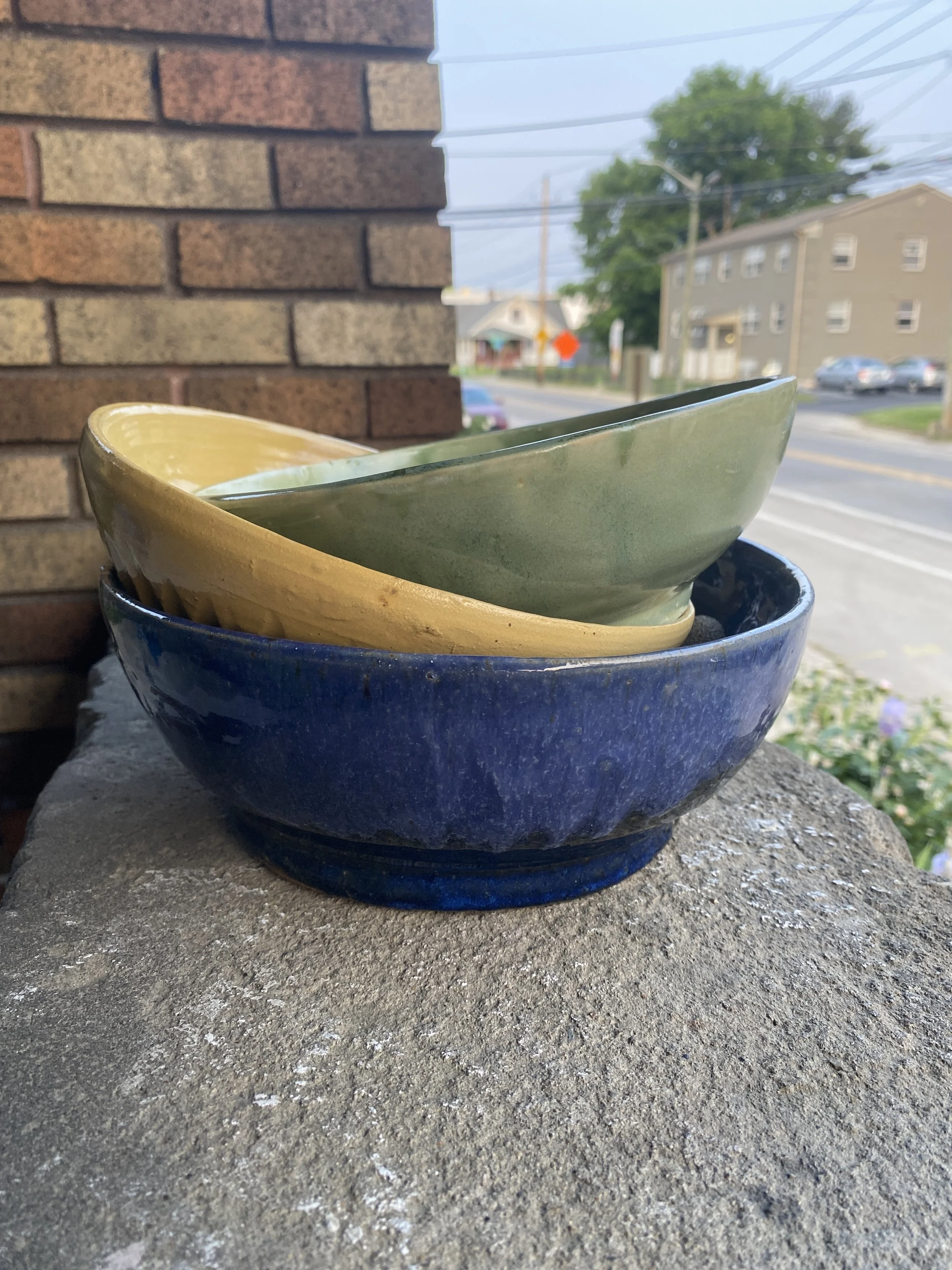 a stack of handmade bowls by london heist. This ceramic pottery set is made of kentucky mudworks and glazes from amaco.  bowls were fired at yellow door ceramics in indianapolis indiana at the milky way complex. blue, green, and yellow bowls
