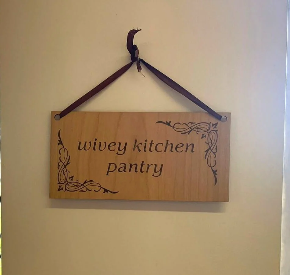 Wooden sign with 'wivey kitchen pantry' carved into it hanging on the wall 