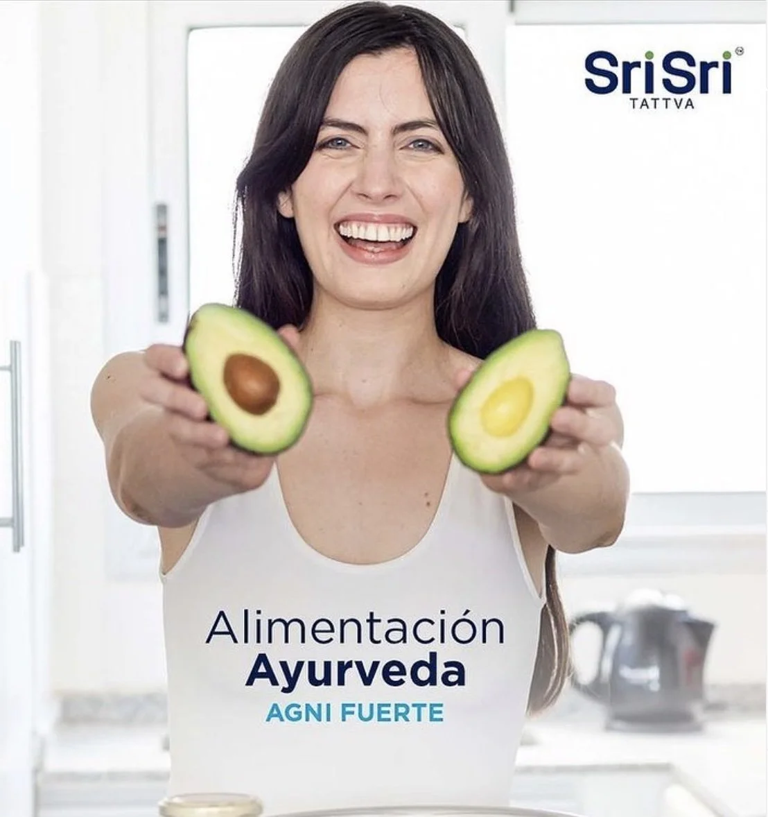 Mujer sonriendo sosteniendo aguacates partidos por la mitad en una cocina moderna.