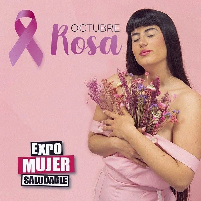 Una mujer con cabello negro y corte de flequillo, con los ojos cerrados, sosteniendo un ramo de flores moradas y rosadas, vestida con ropa rosa, en un fondo rosa claro. En la imagen hay un lazo morado y texto que dice 'Octubre Rosa', 'Exposición Muje