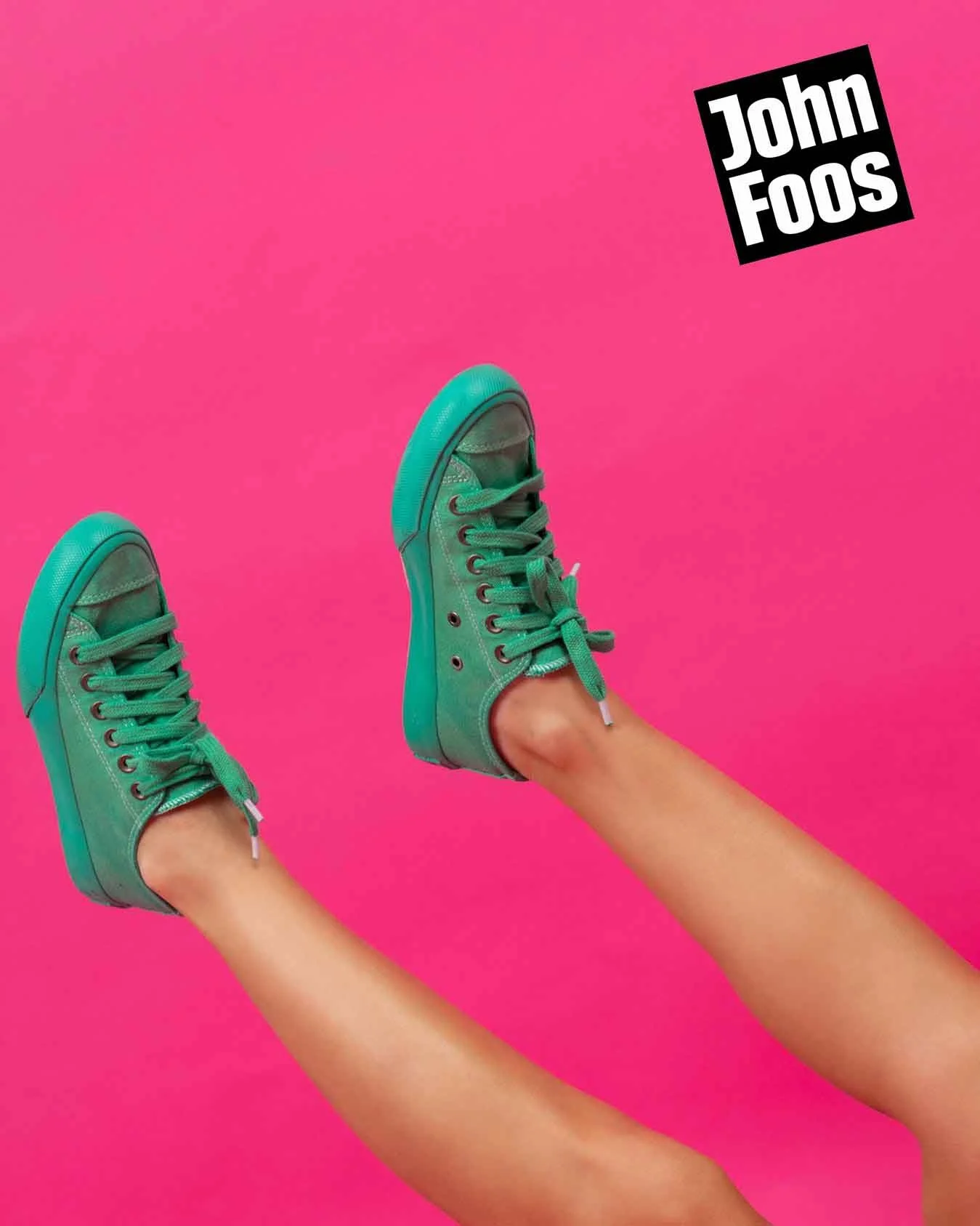 Piernas con zapatos deportivos verdes, fondo rosa brillante, texto 'John Foos' en esquina superior derecha.