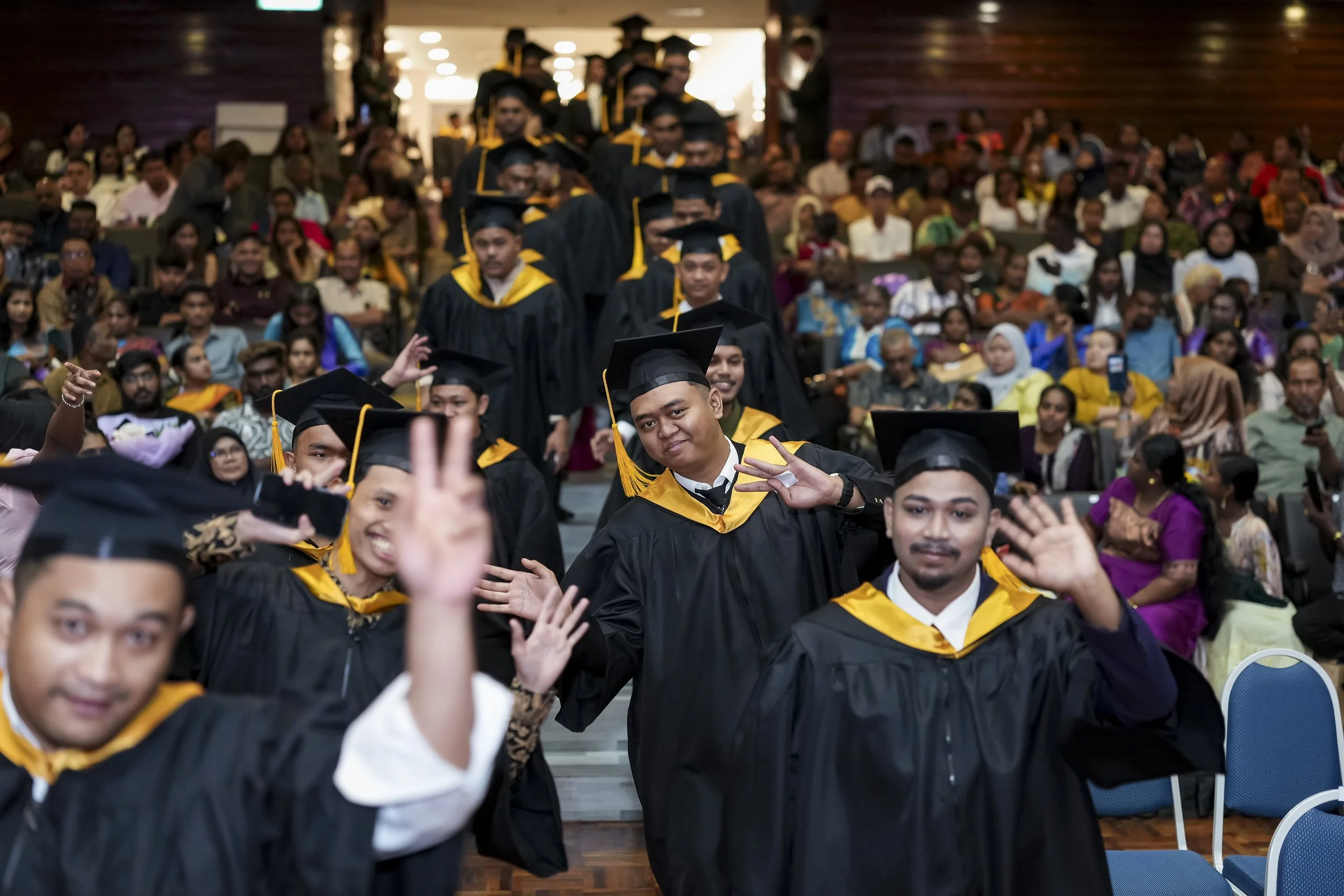 Celebrating graduation with graduates in black caps and gowns, smiling and posing for photos in a crowded indoor setting.