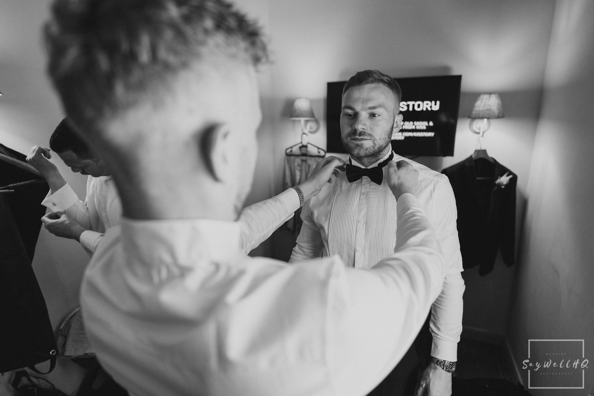 Groom getting help putting on his bow tie before his wedding at Doddington hall