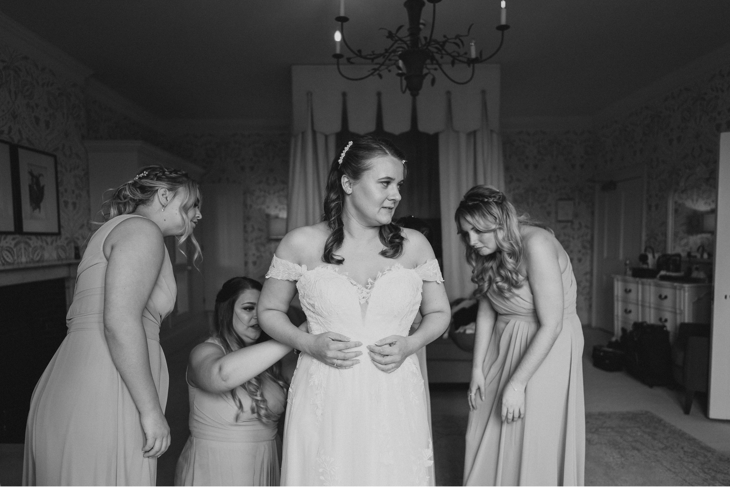 HODSOCK PRIORY WEDDING PHOTOGRAPHY - bride getting help from her bridesmaids in putting the wedding dress on