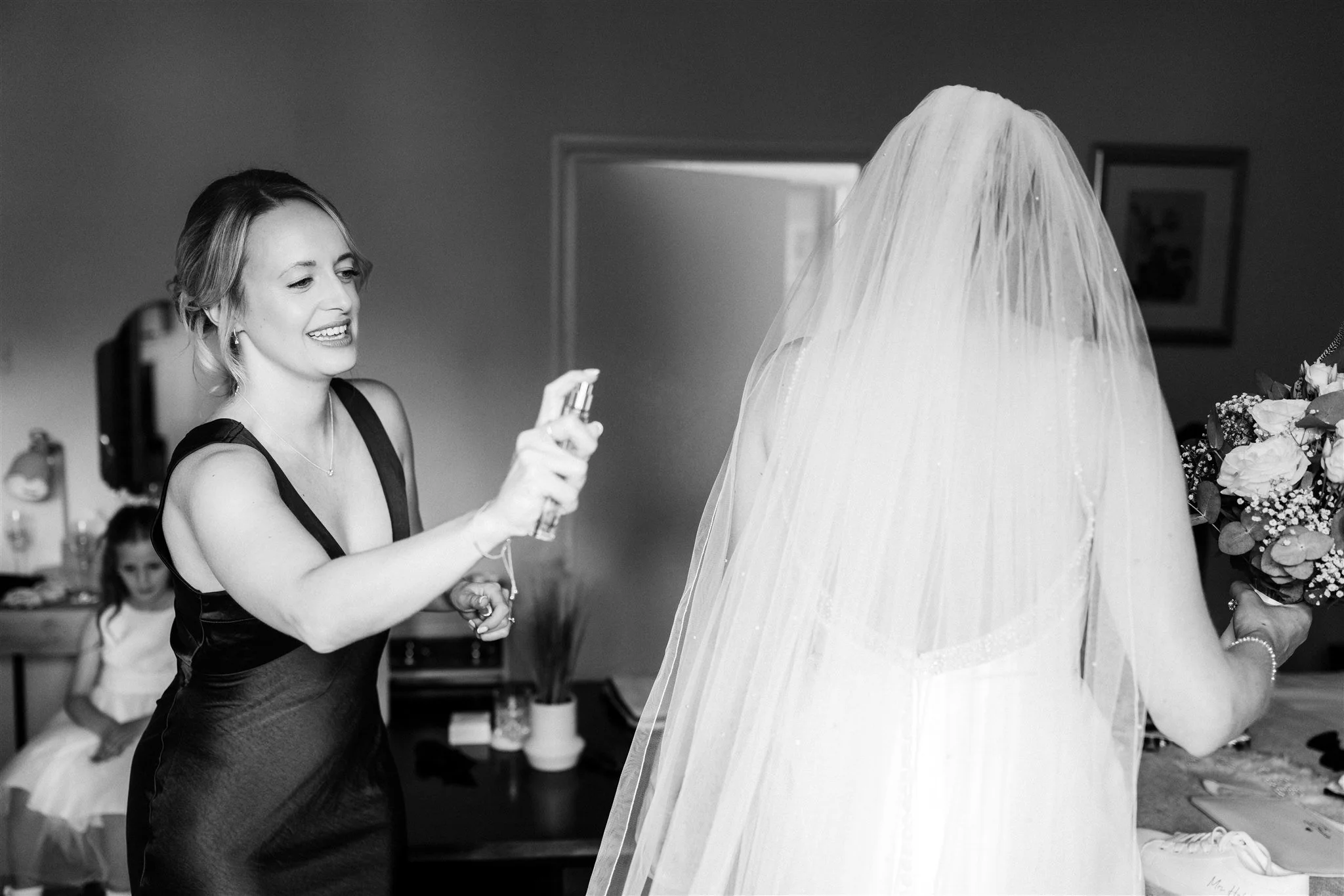 Bridesmaids spraying the bride with perfume on the morning of her wedding at Woodborough Hall