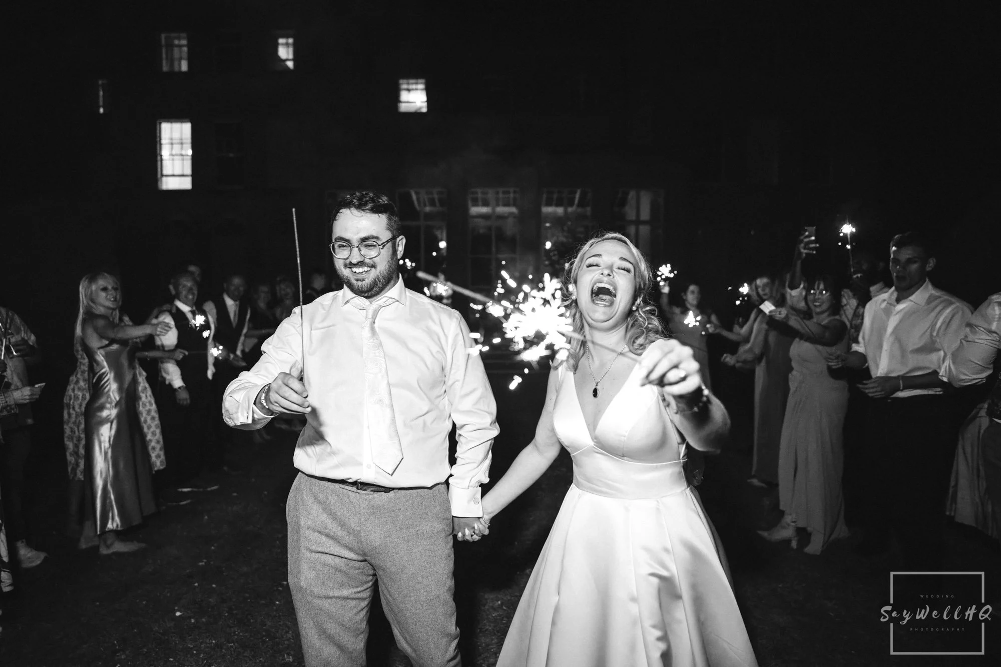 Bride and groom enjoying a fun sparkler exit at night during their wedding at Prestwold Hall – candid, relaxed wedding photography by SaywellHQ.co.uk.