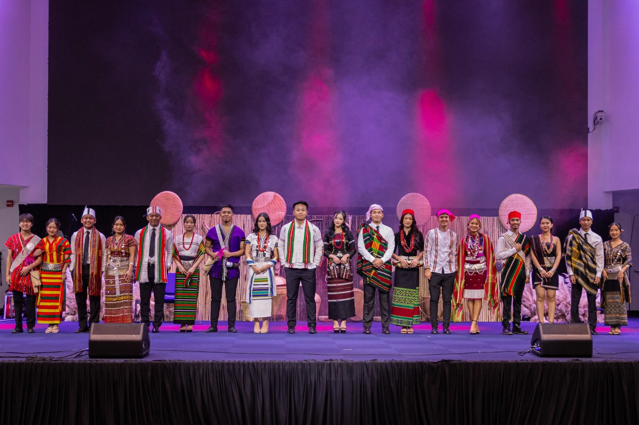 Group of people dressed in traditional ethnic attire standing on stage during a cultural performance.