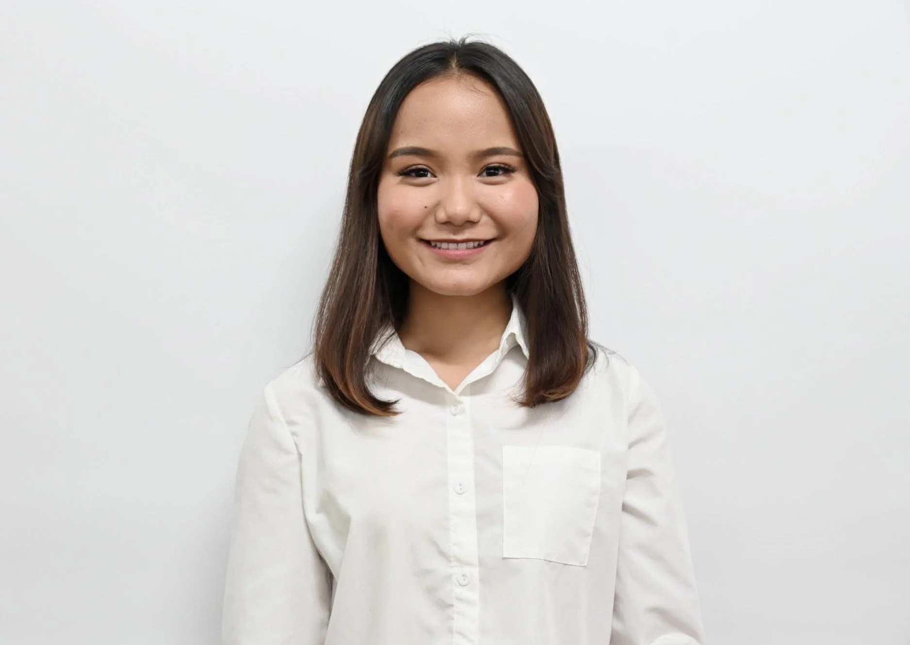 A woman with long black hair wearing a black collared shirt, smiling faintly against a white background.