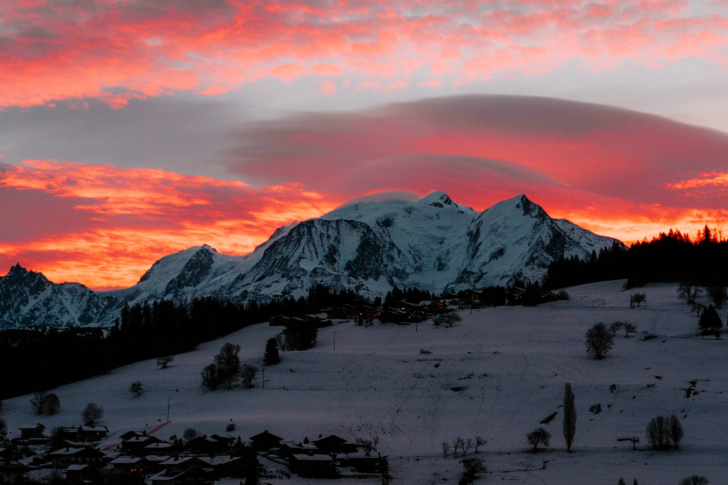 Een berglandschap met een besneeuwde berg onder een kleurrijke oranje en roze sunset