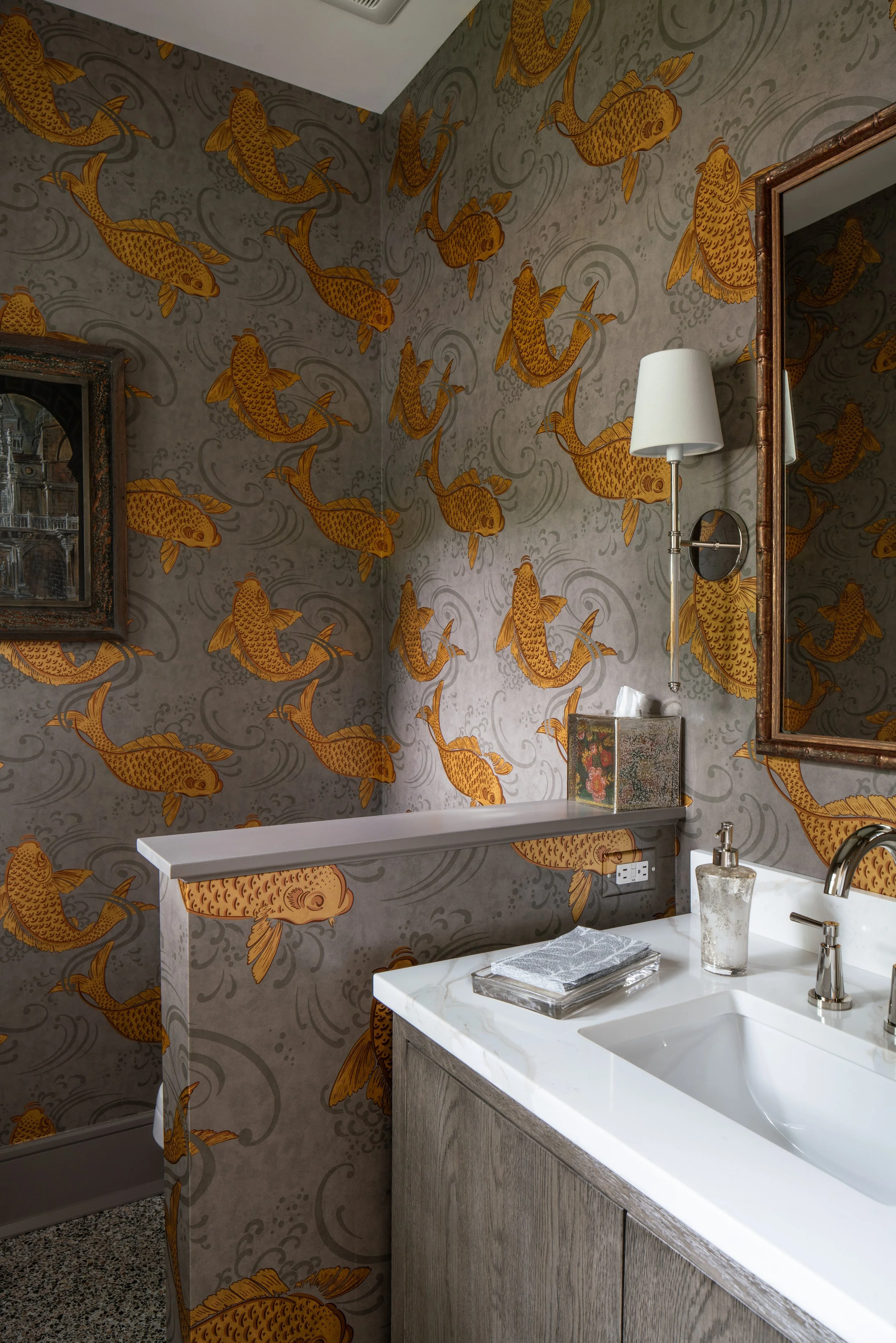 Bathroom with wallpaper featuring goldfish swimming in water, white countertop with sink, soap dispenser, mirror, wall-mounted lamp, tissue box, and folded towels.