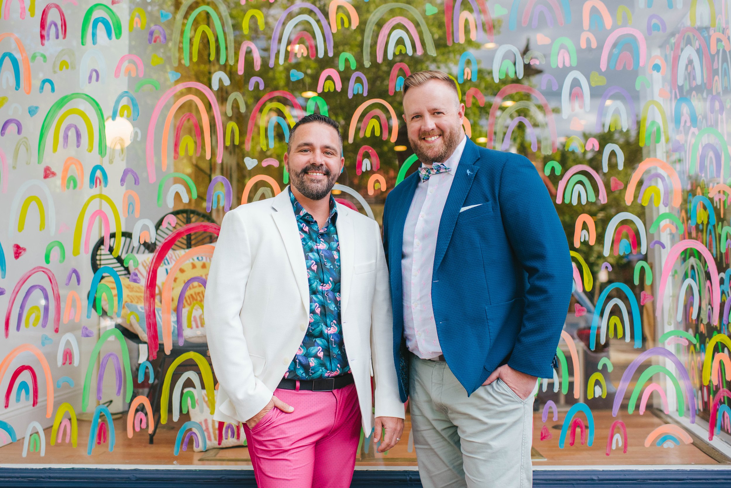 a photo of JFKLiving's Founders Jeremiah Kobelka on the left, and Pip Haxby-Thompson on the right. Two of South Jersey's best real estate agents. Both wear smartwear, and they are stood in front of the rainbow-covered shopfront of Occasionette