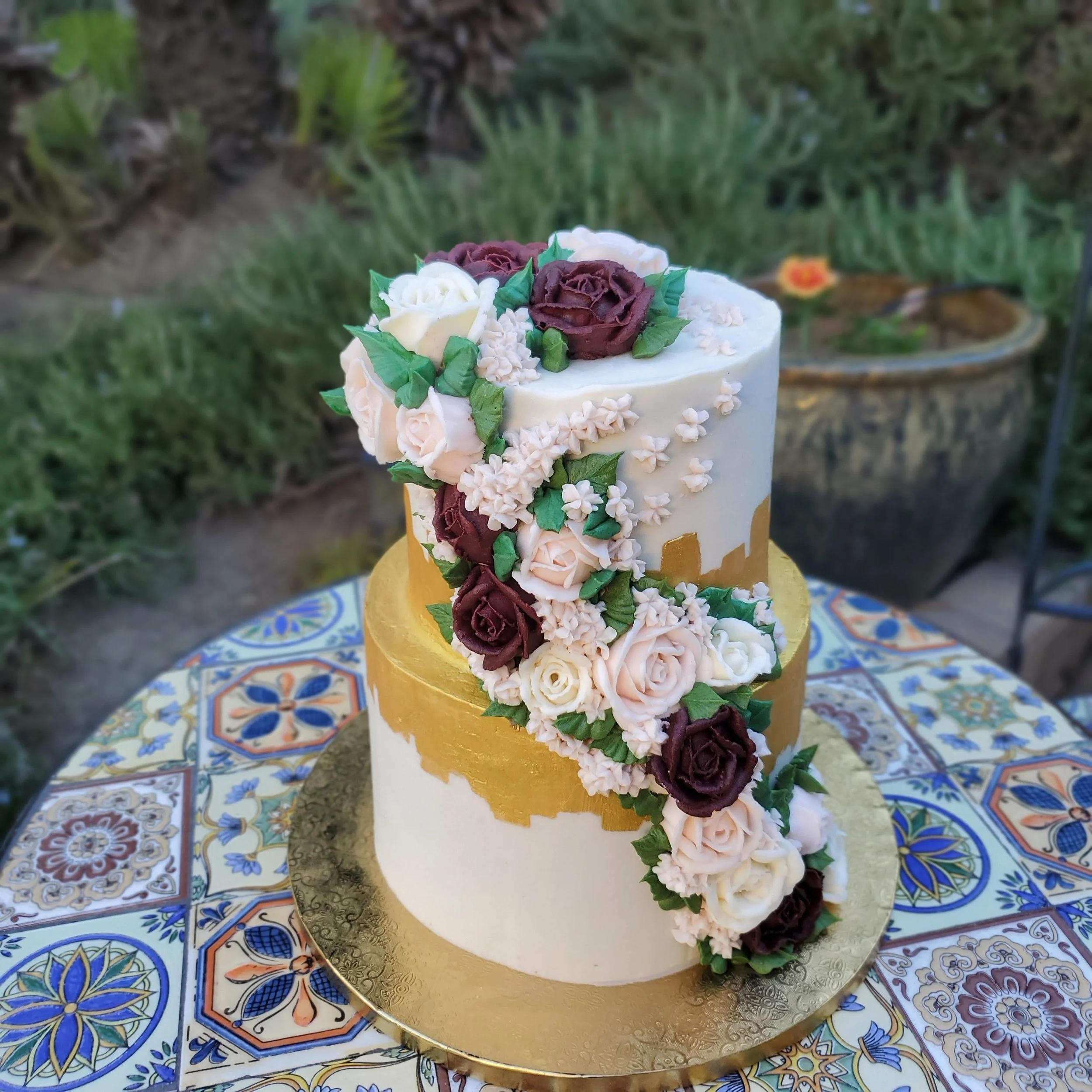 floral tiered cake with burgundy, blush pink, and white roses and gold detailing