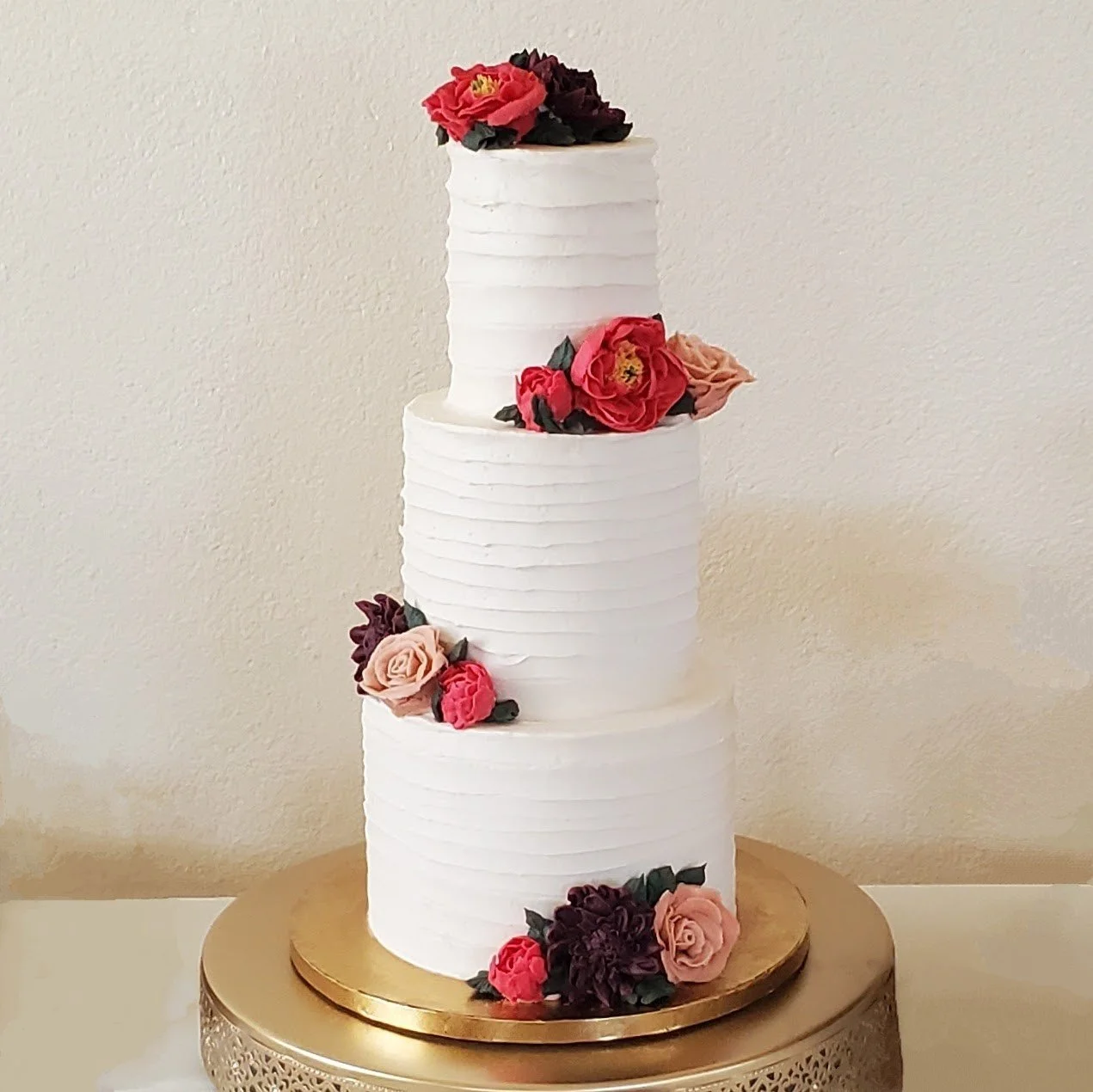 white three tiered wedding cake with jewel toned buttercream flowers