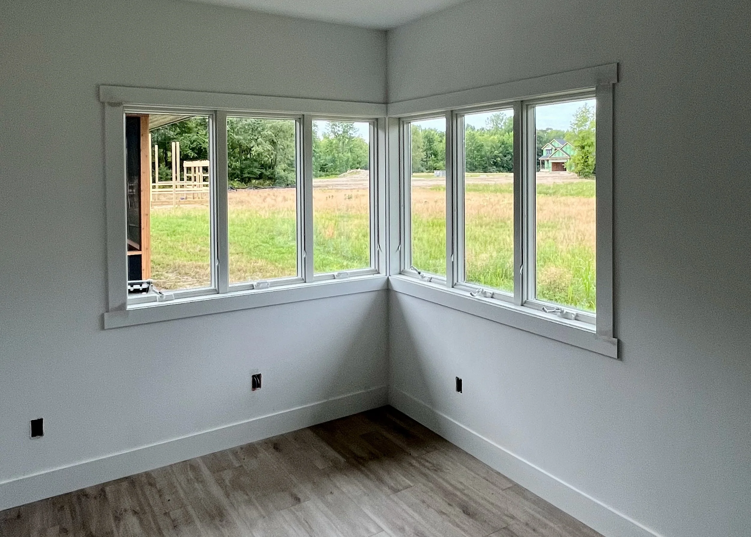 View of an empty field looking out windows in the corner of a room.
